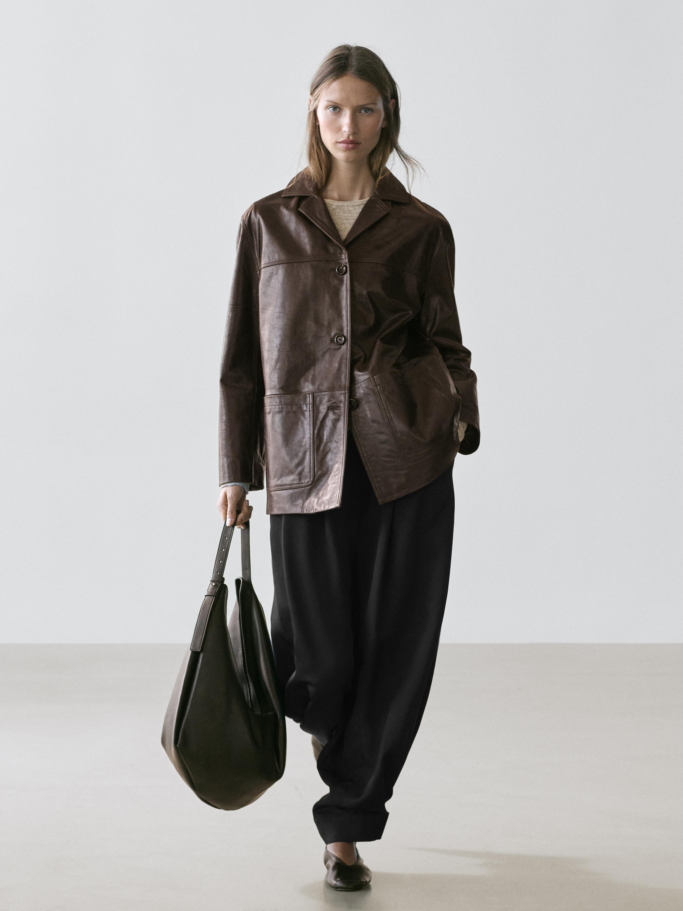 Conjunto de chaqueta marrón con botones y bolsillos frontales, pantalones negros amplios y bolso grande marrón.