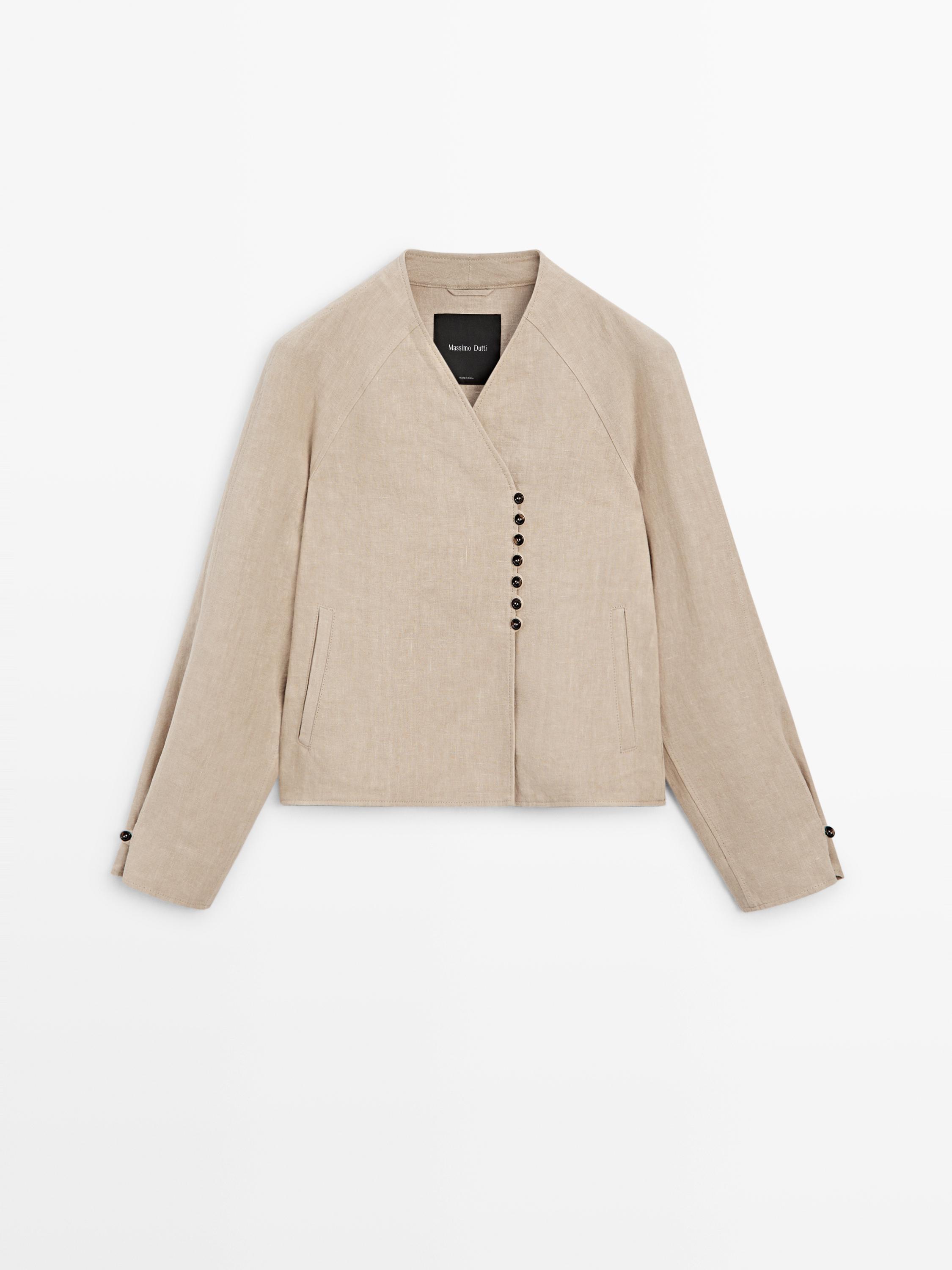 Front view of a beige jacket with asymmetrical black buttoning and side pockets.