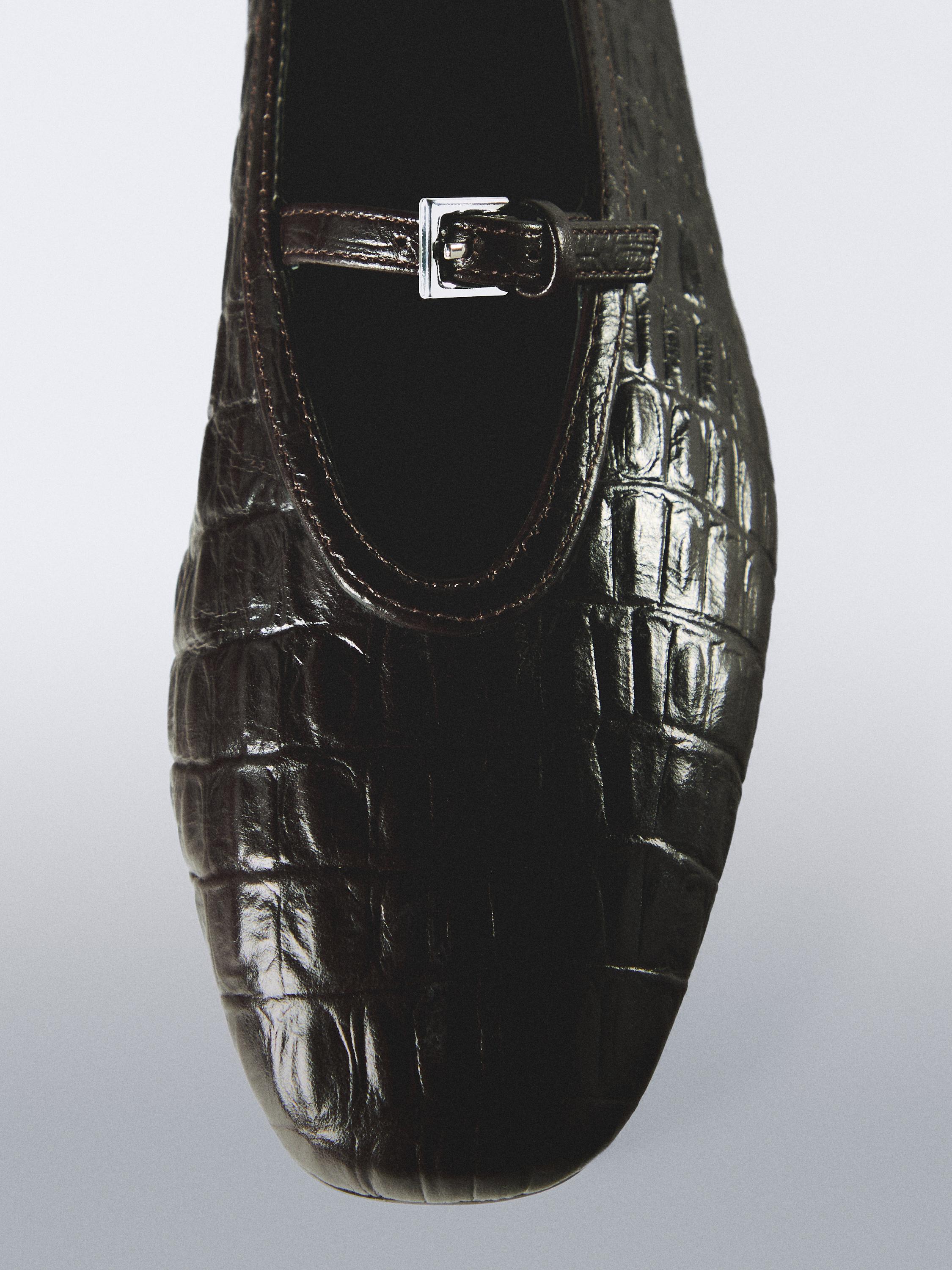 Detalle de bailarina marrón con textura de cocodrilo y hebilla metálica en la parte superior.
