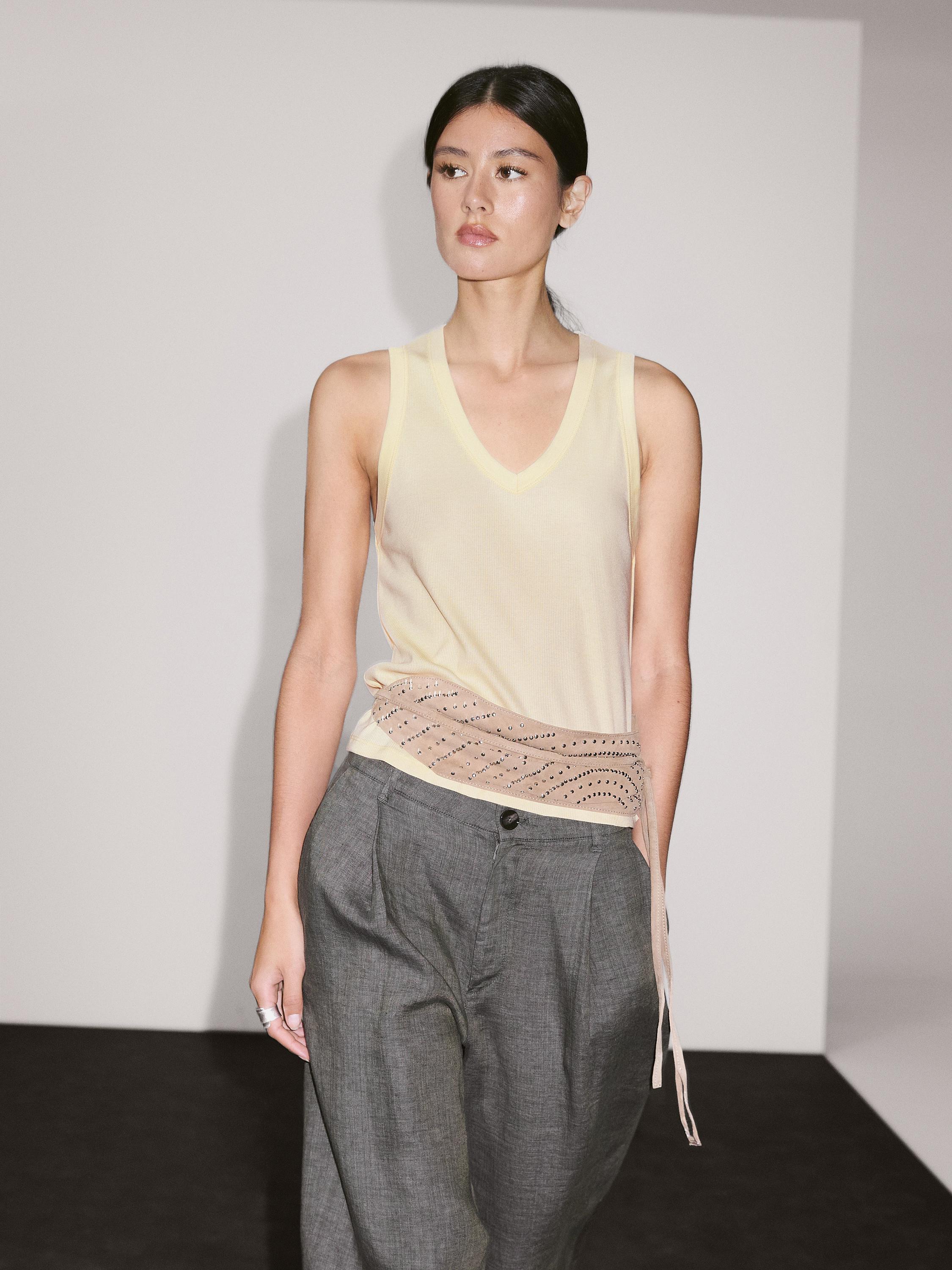 Ensemble composé d'un débardeur écru à col en V avec ceinture beige perforée et d'un pantalon gris à coupe ample.