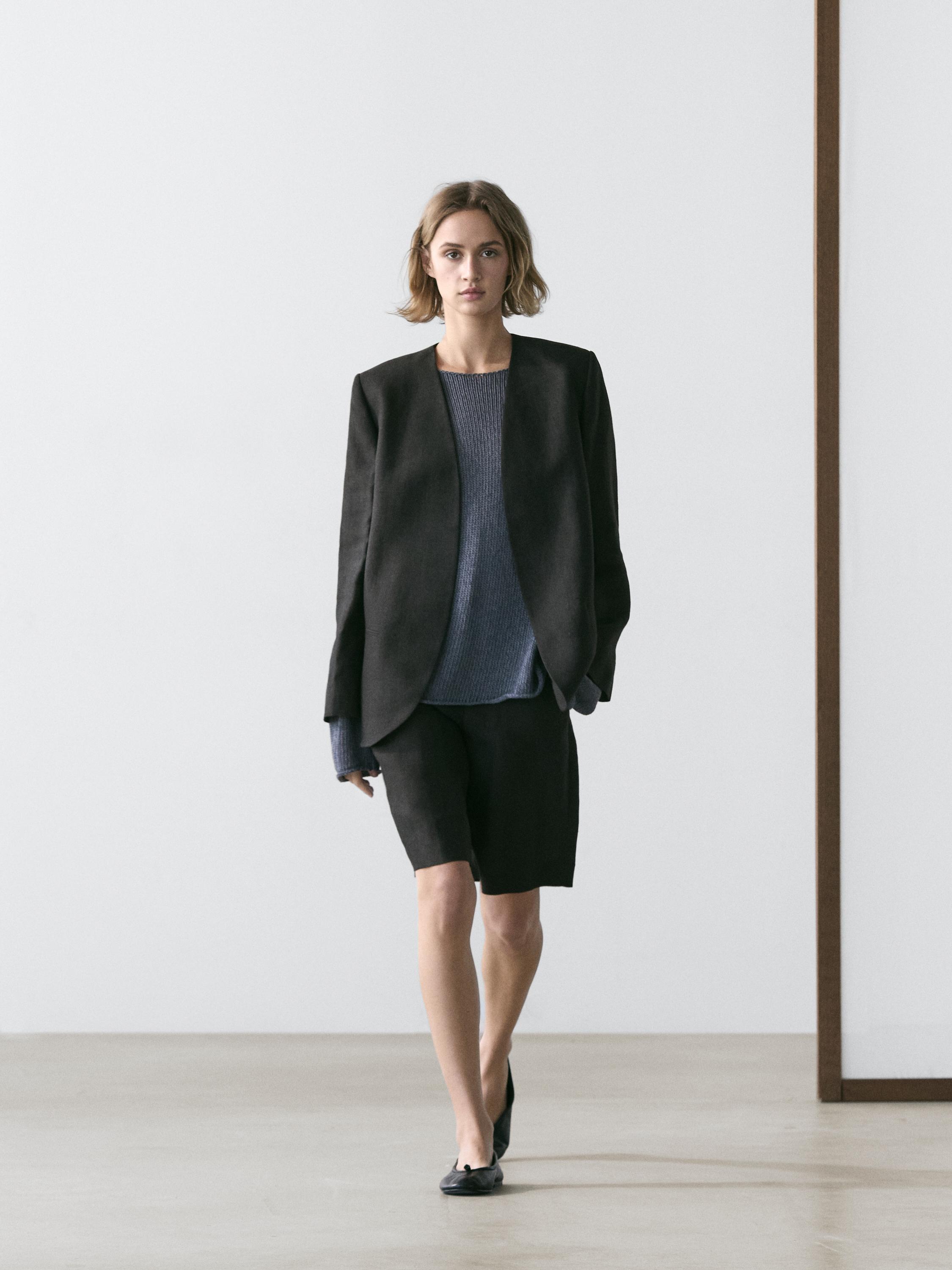 Black blazer set without lapels, blue sweater, and black Bermuda shorts.