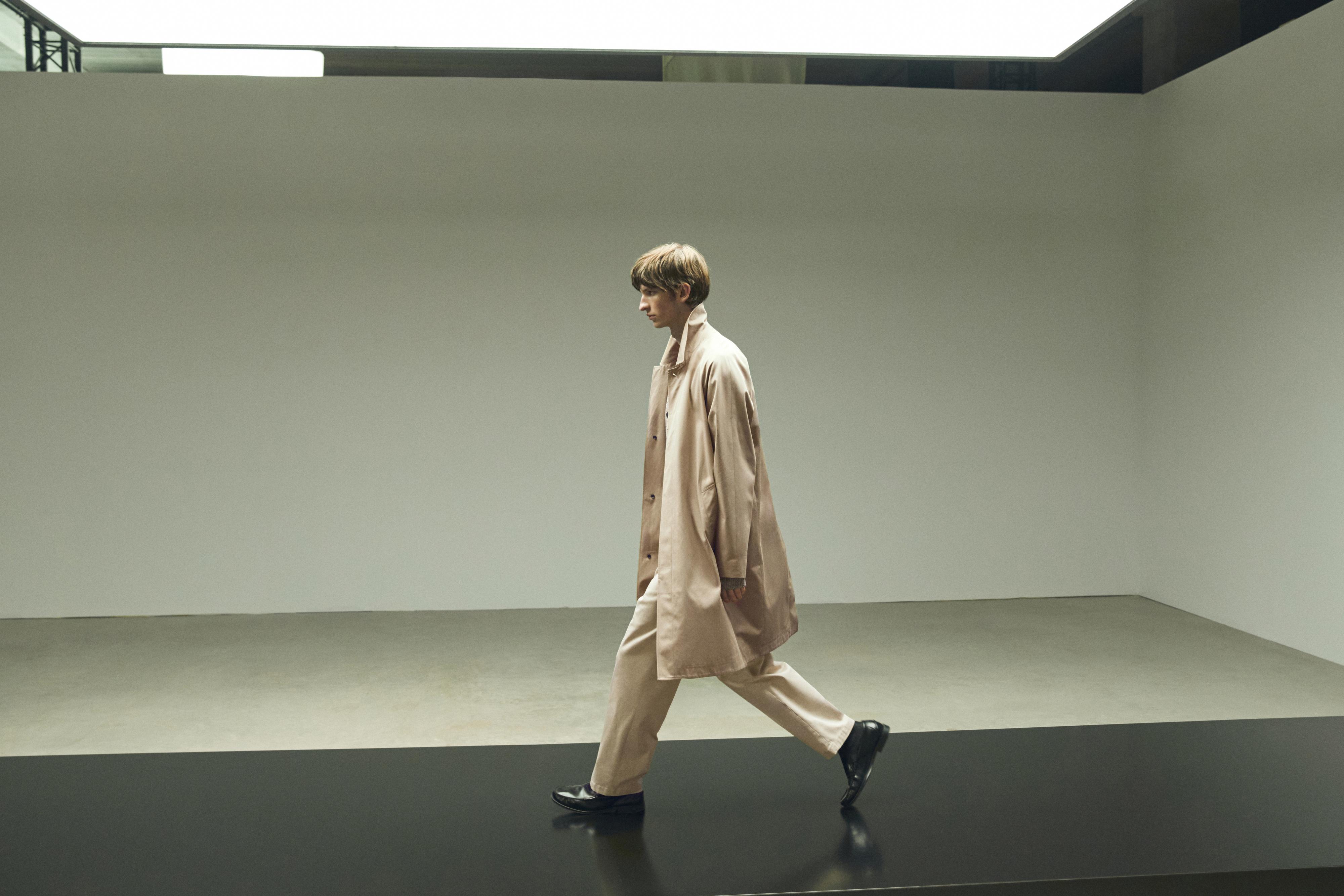 버튼 디테일의 베이지색 롱 코트와 어울리는 팬츠 세트, 검은색 신발.