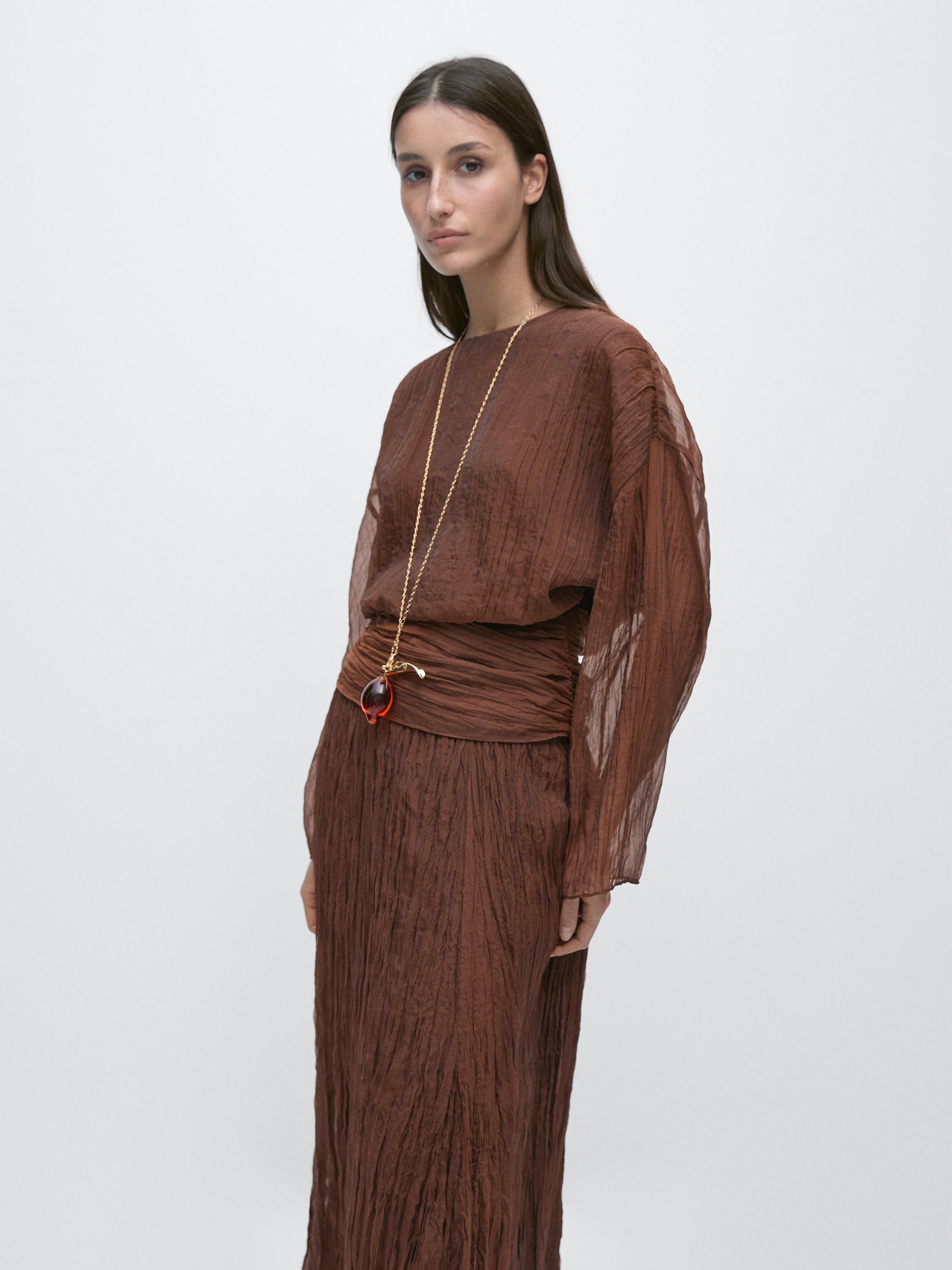 Medium shot of a caramel blouse with a cummerbund and ruched detail, long sleeves, and wrinkled texture.