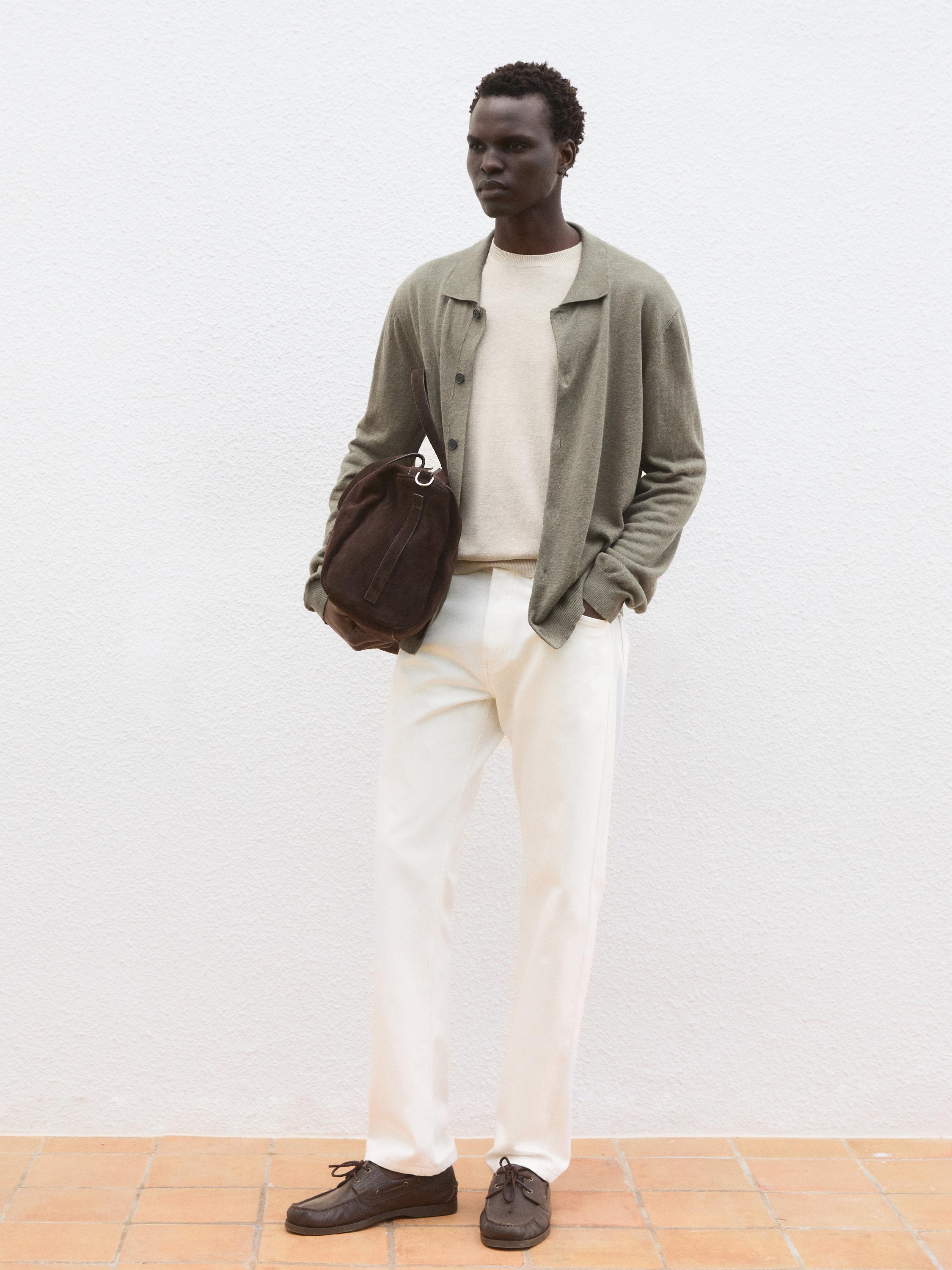 Conjunto de chamarra verde olivo, playera beige y pantalón blanco. Zapatos café y bolsa café oscuro.