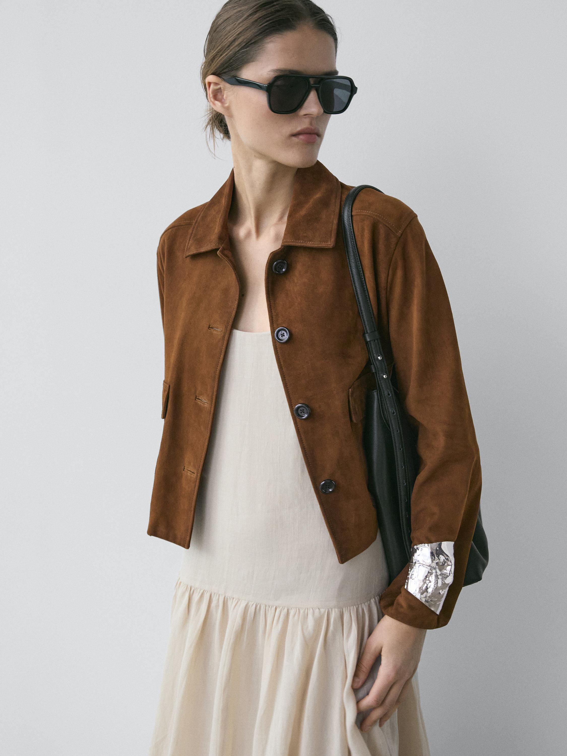 Braunes Bomberjacken-Set mit Knöpfen und Seitentaschen, über beigem Kleid. Metalldetail am Ärmel.