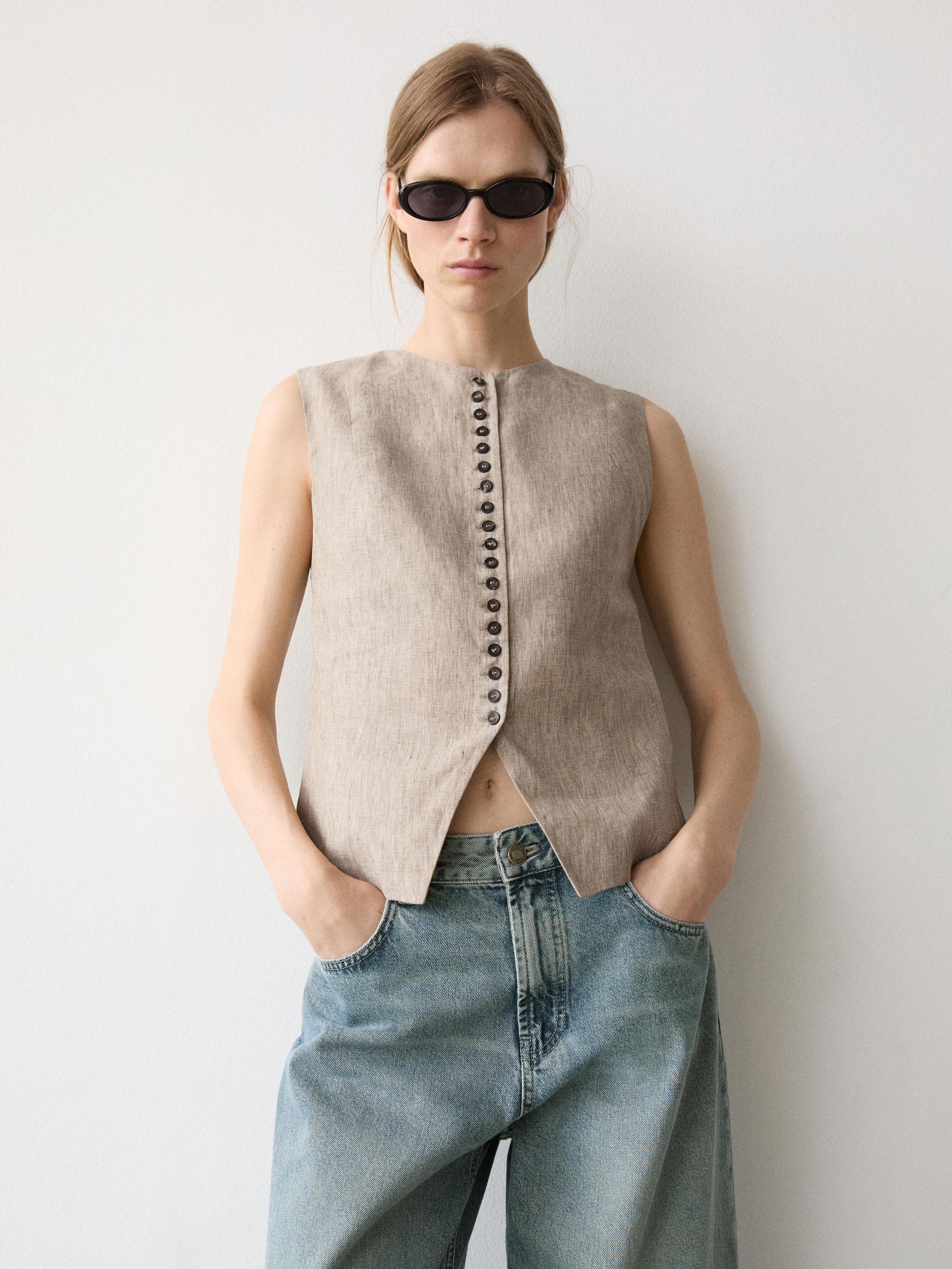 Beiges, ärmelloses Westenset mit Knopfleiste vorne und blauen Jeans mit Seitentaschen.