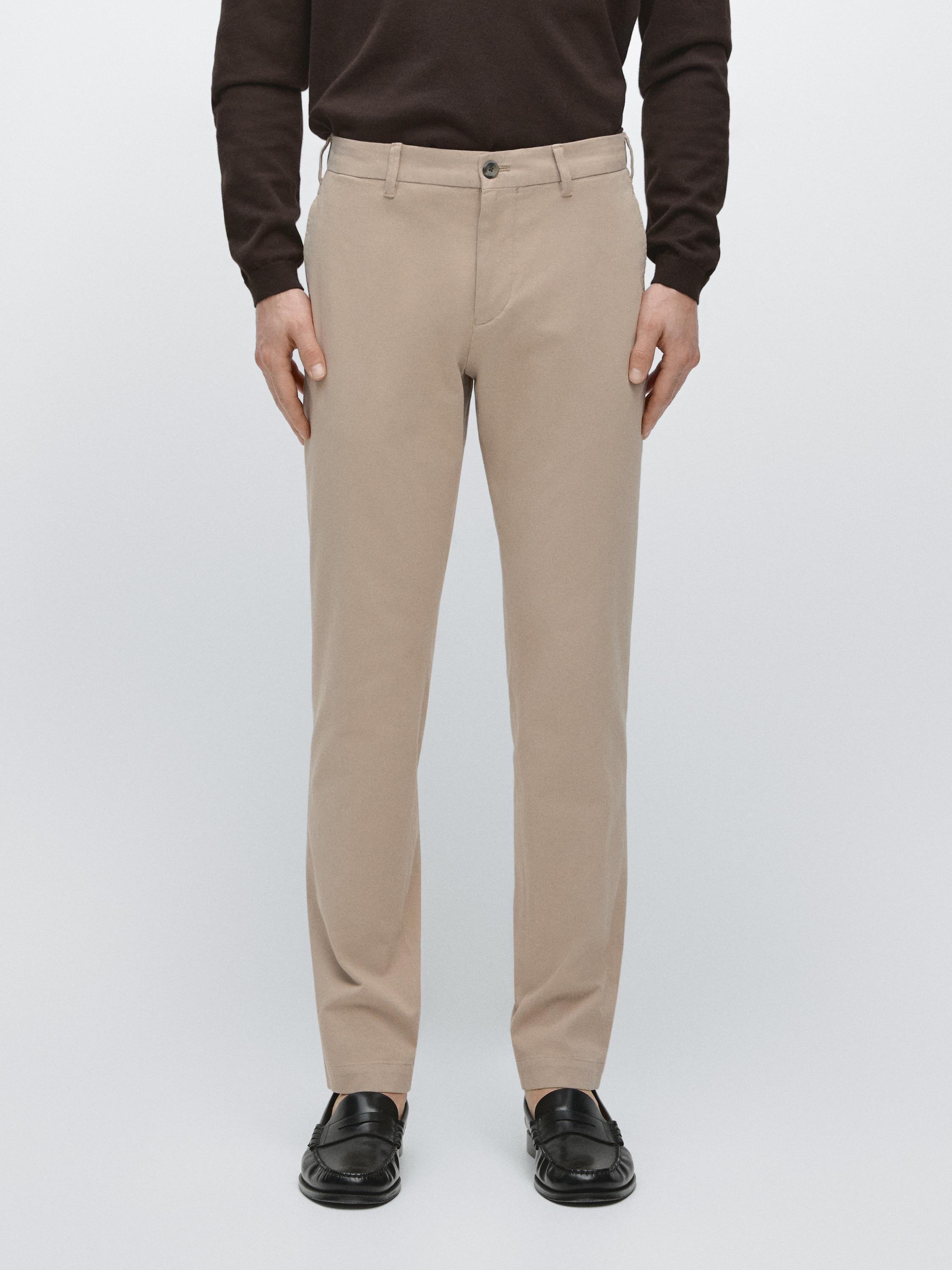 Ensemble de pantalon beige slim fit avec poches latérales et bouton frontal, combiné avec des chaussures noires.