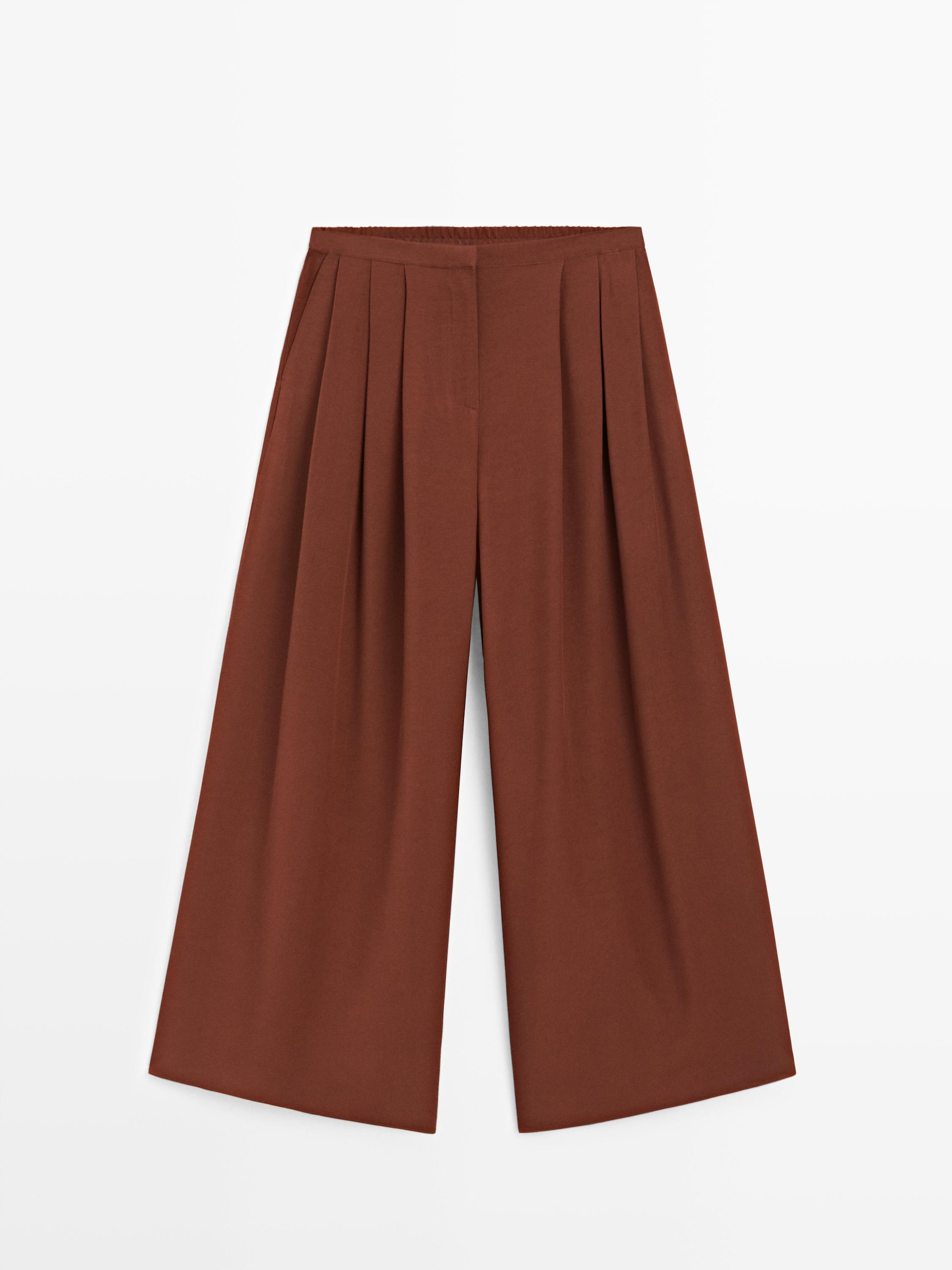 Front view of orange wide-leg pants with pleats and elastic waist.