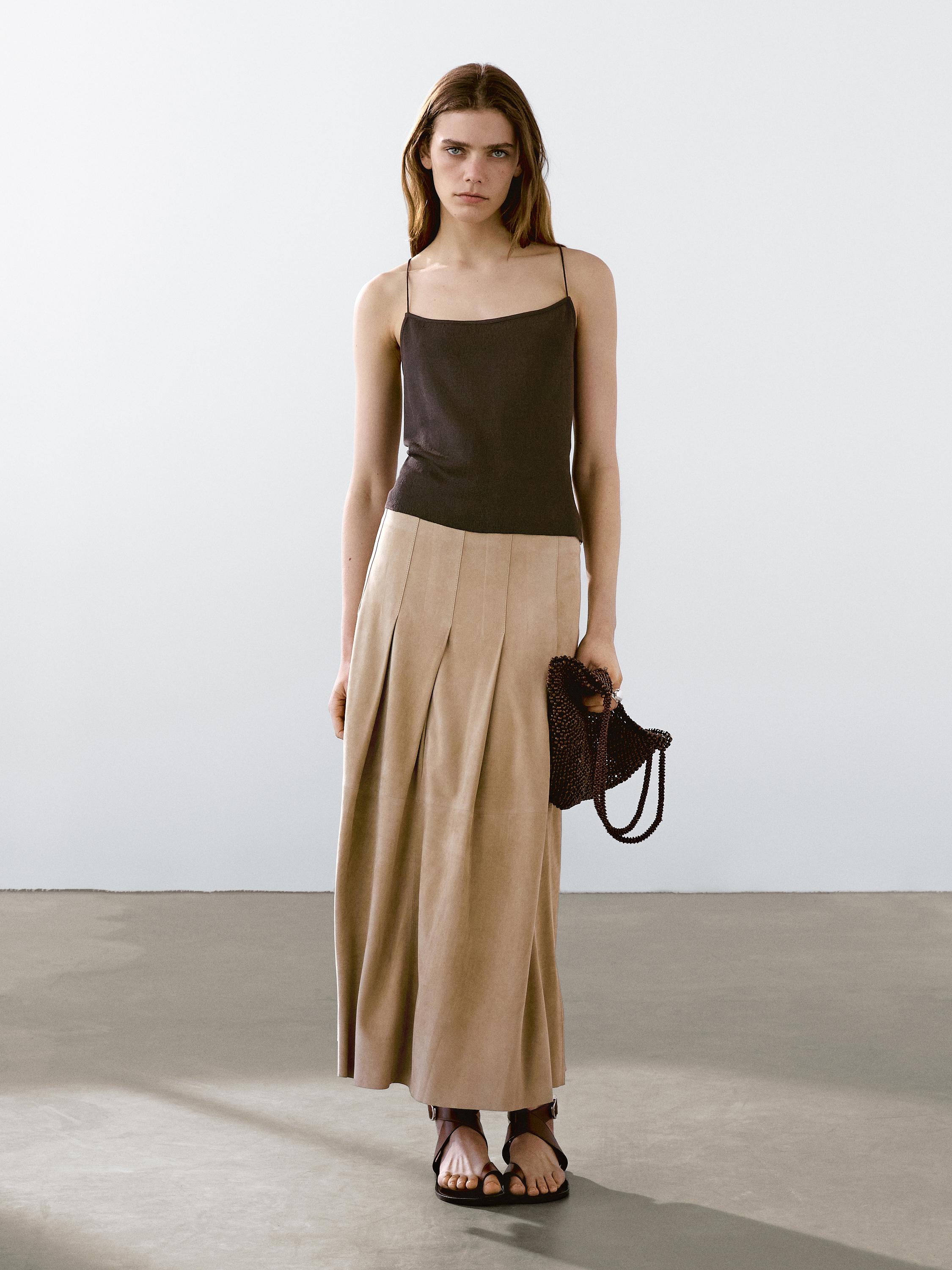 طقم مكون من توب أسود بحمالات وتنورة بيج طويلة بكسرات مع حقيبة بنية اللون وصندل.