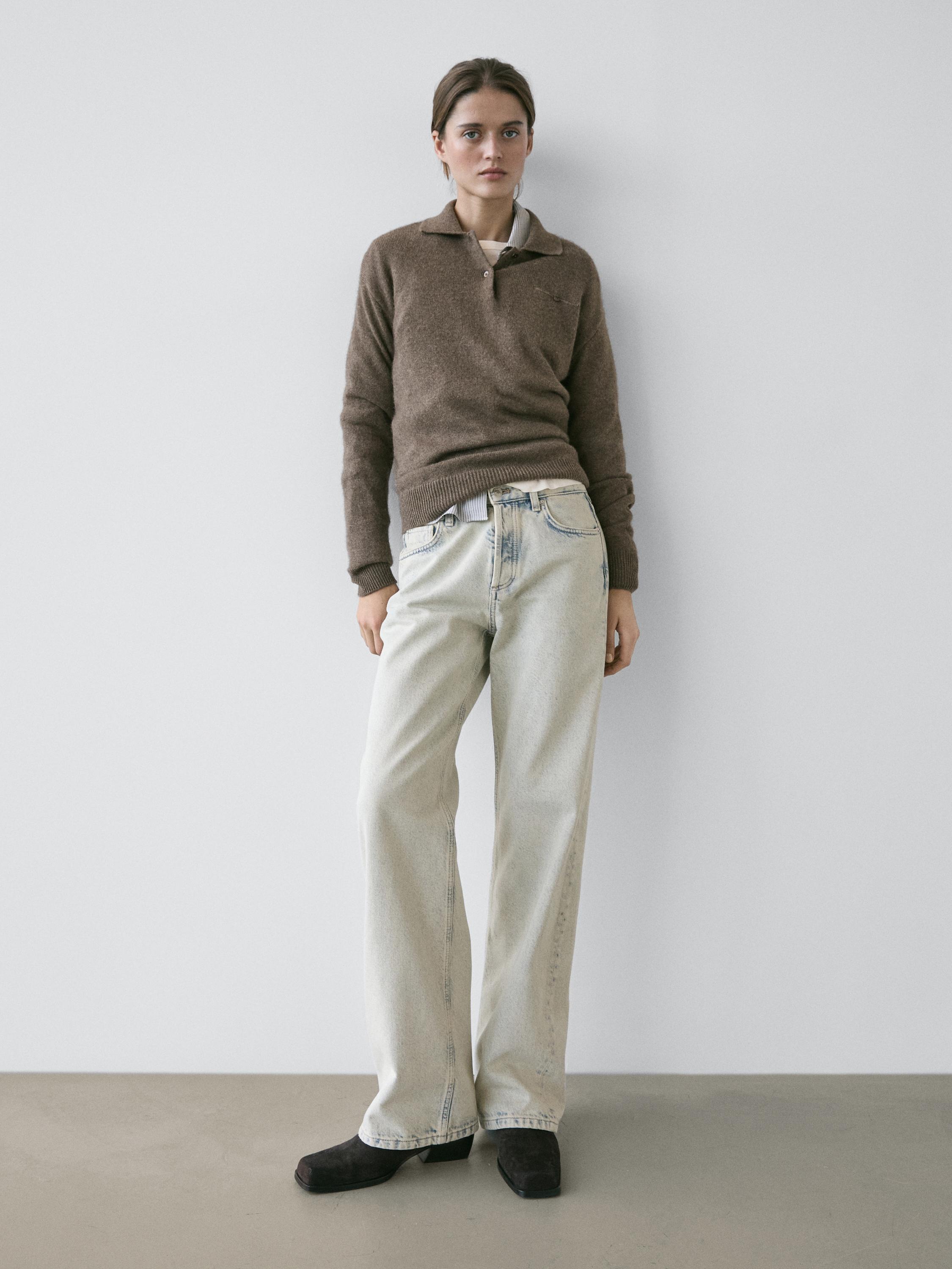 طقم سويتر بني بياقة وأزرار، جينز فاتح بقصة مستقيمة وحذاء أسود.