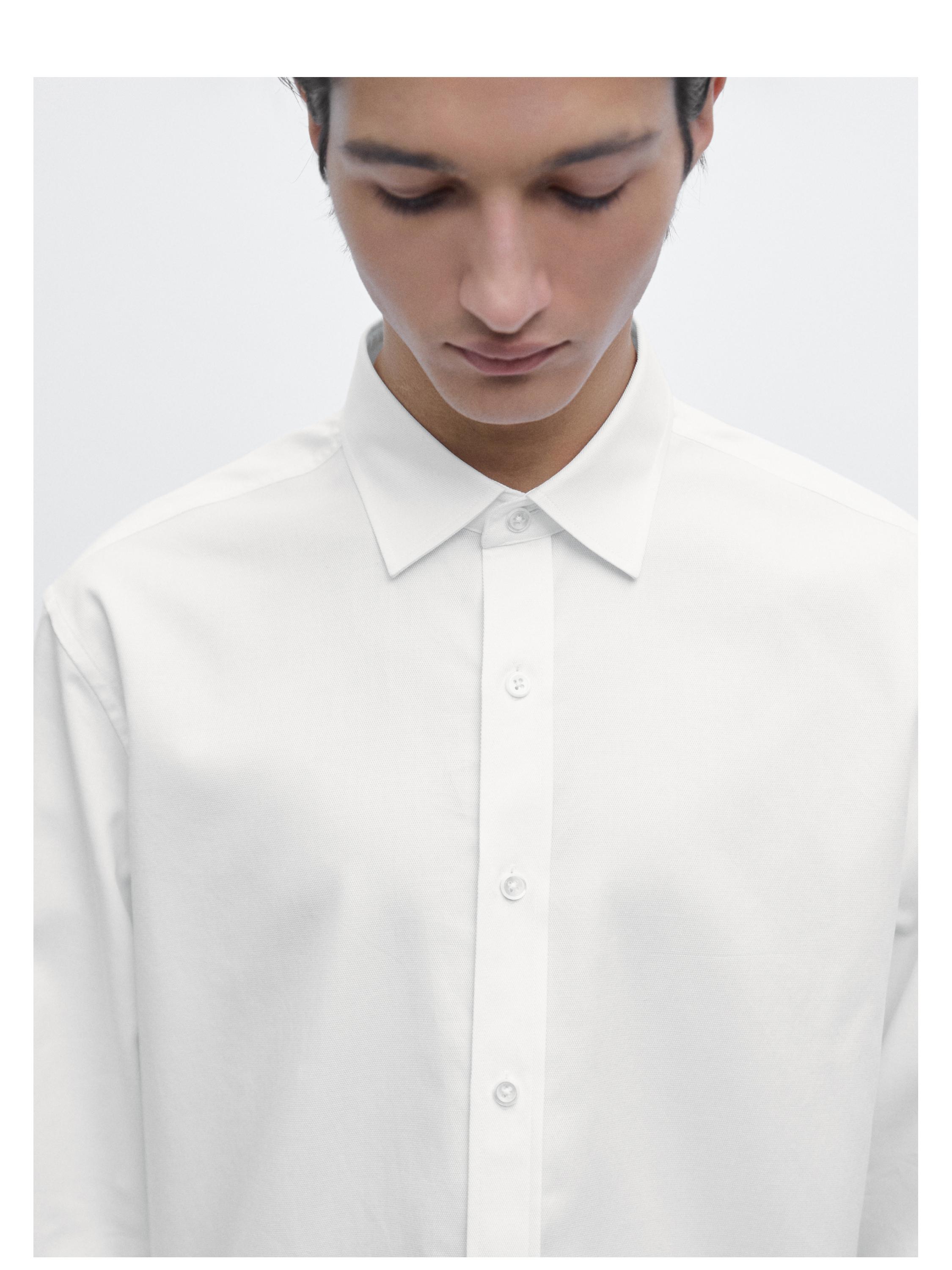 Mellembillede af hvid langærmet skjorte med klassisk krave og knaplukning foran.