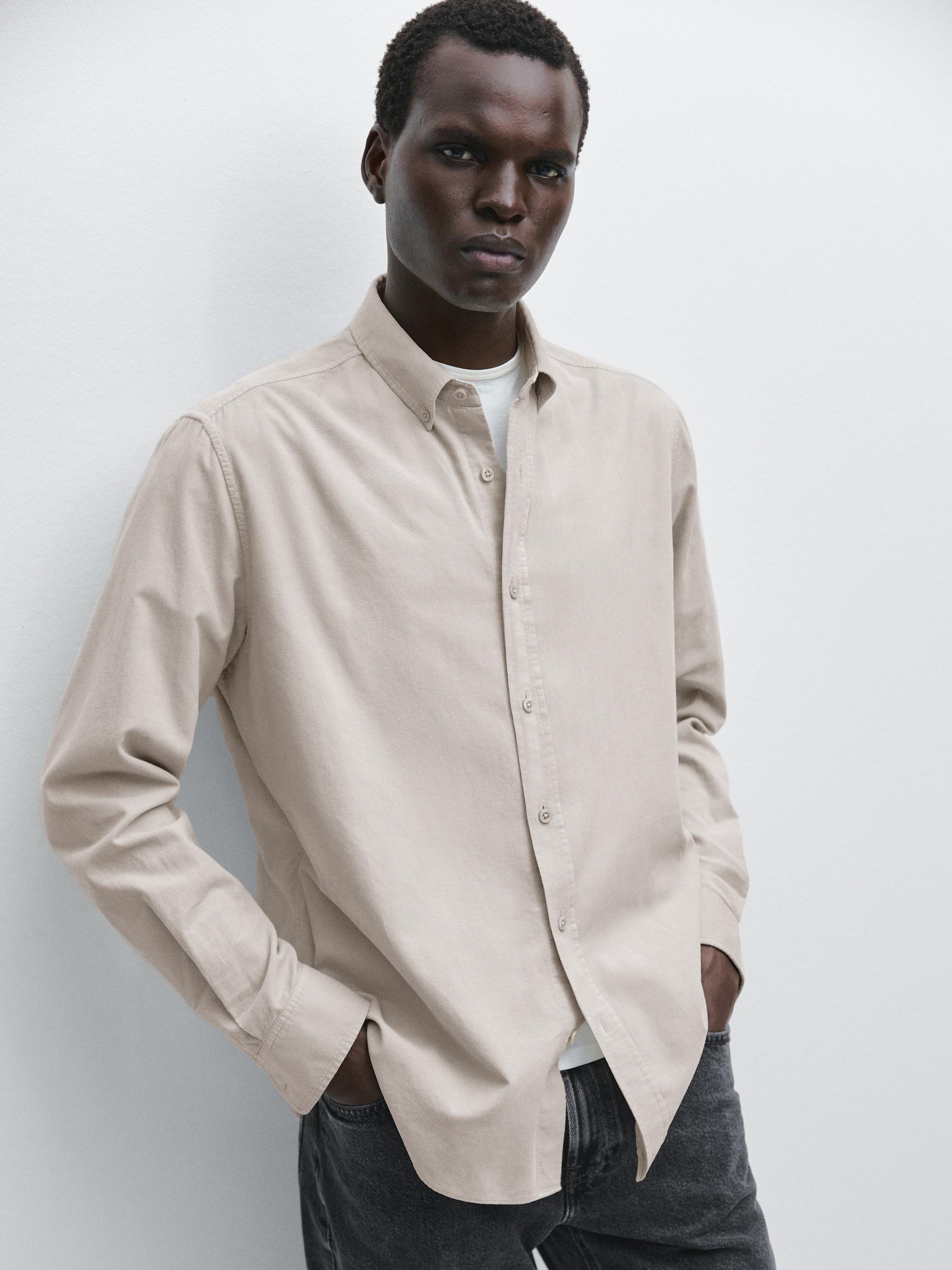 Ensemble de chemise sable à manches longues boutonnée et pantalon foncé.