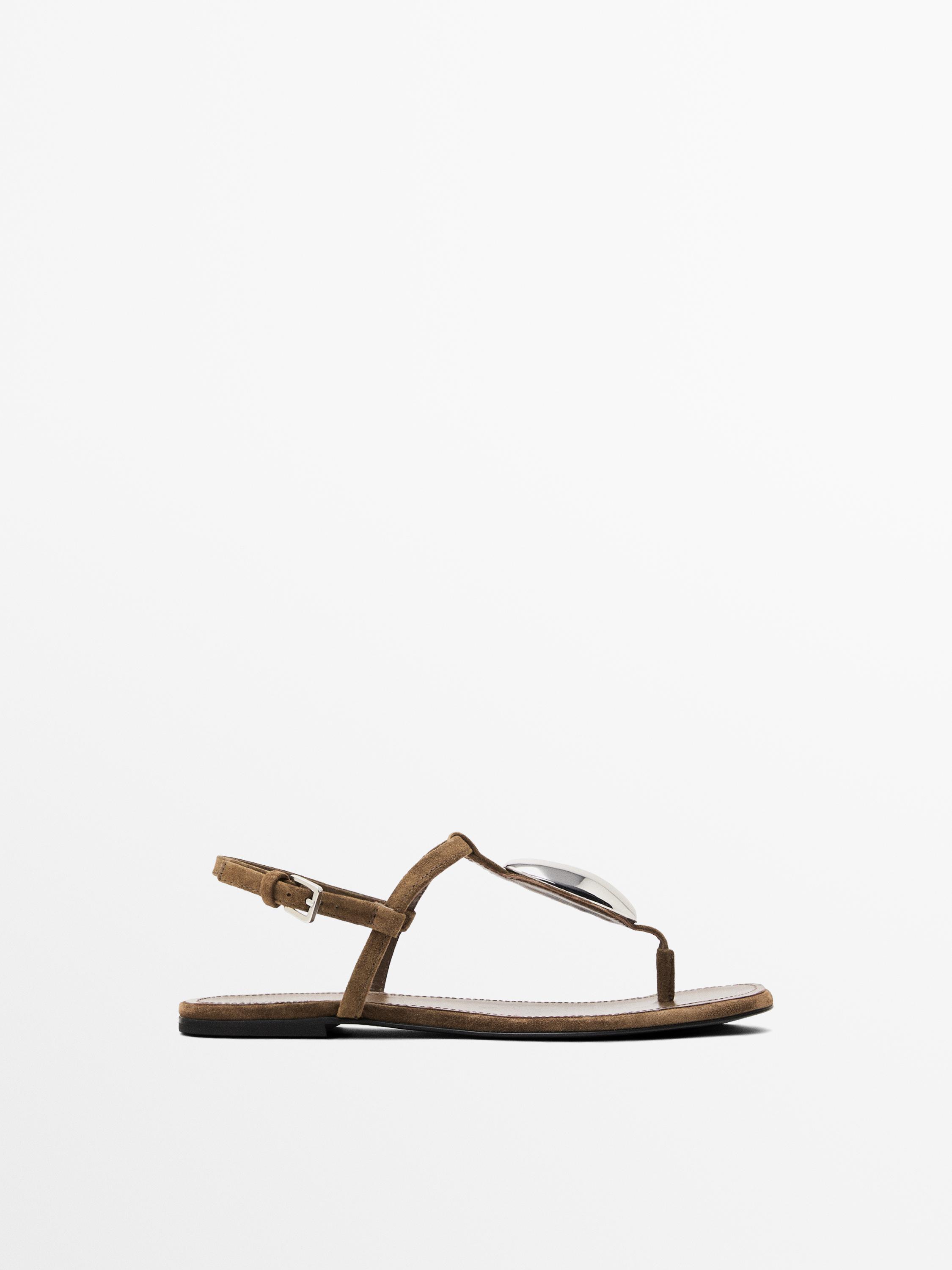 Side view of a brown flat sandal with metallic detailing on the front strap and adjustable buckle fastening at the ankle.