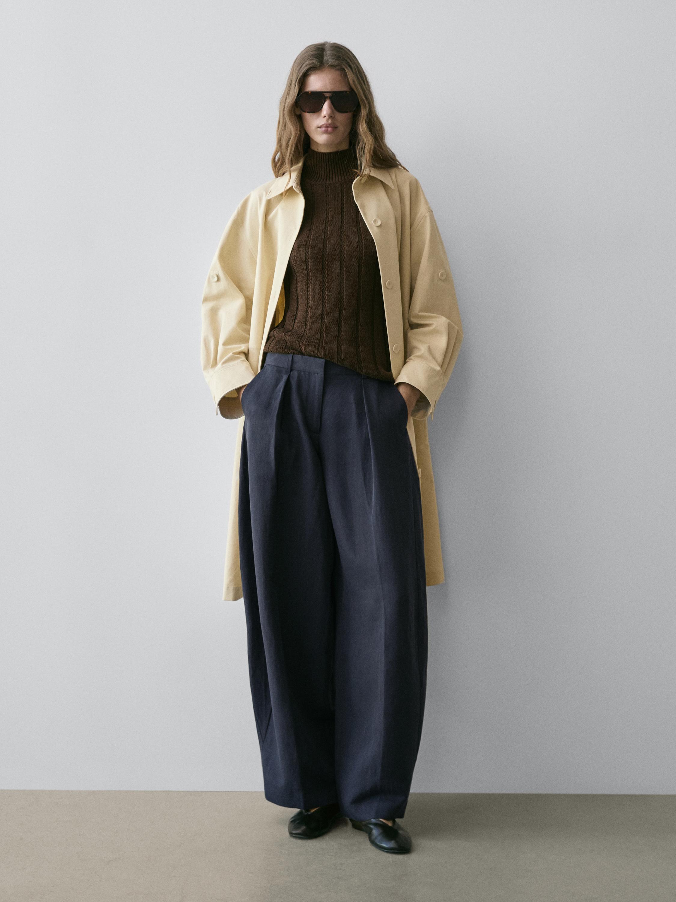 Beige mantelpak, bruine coltrui en een soepelvallende marineblauwe broek met plooien.