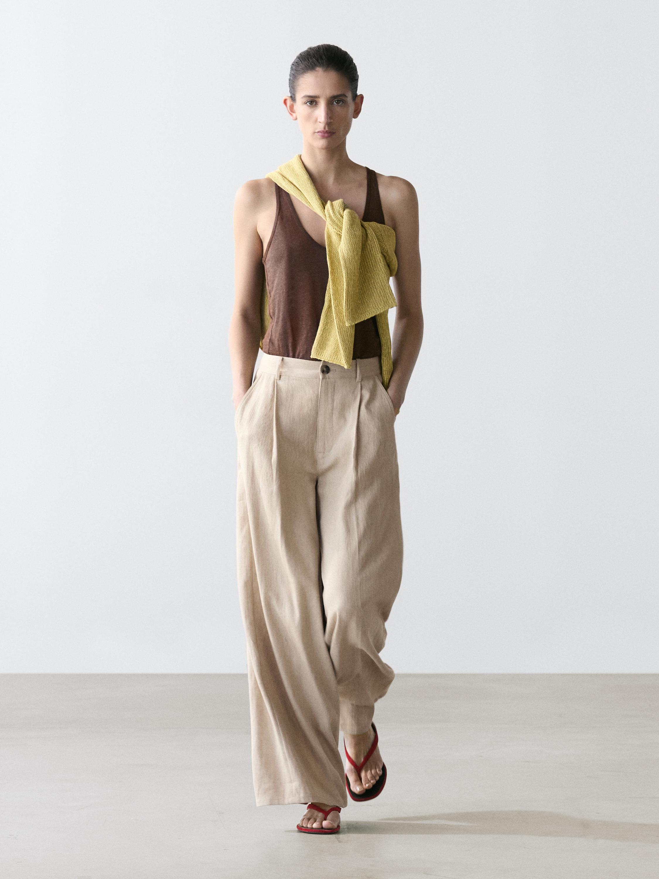 Ensemble composé d'un pantalon couleur sable taille haute et coupe ample avec poches latérales, d'un t-shirt marron et d'un pull jaune porté sur les épaules.