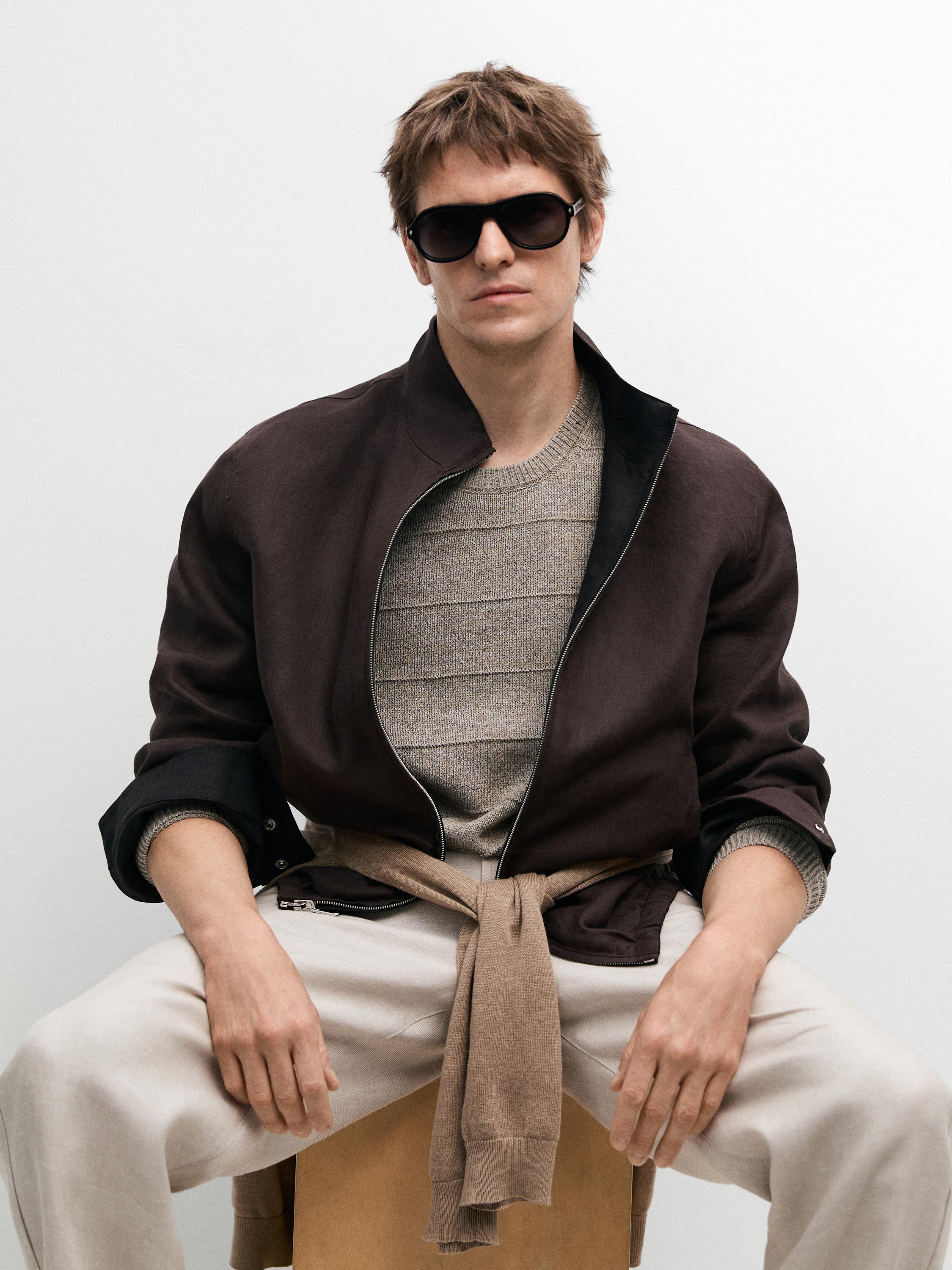 Conjunto de cazadora negra con cremallera, suéter gris de rayas y pantalones claros. Suéter marrón atado a la cintura.