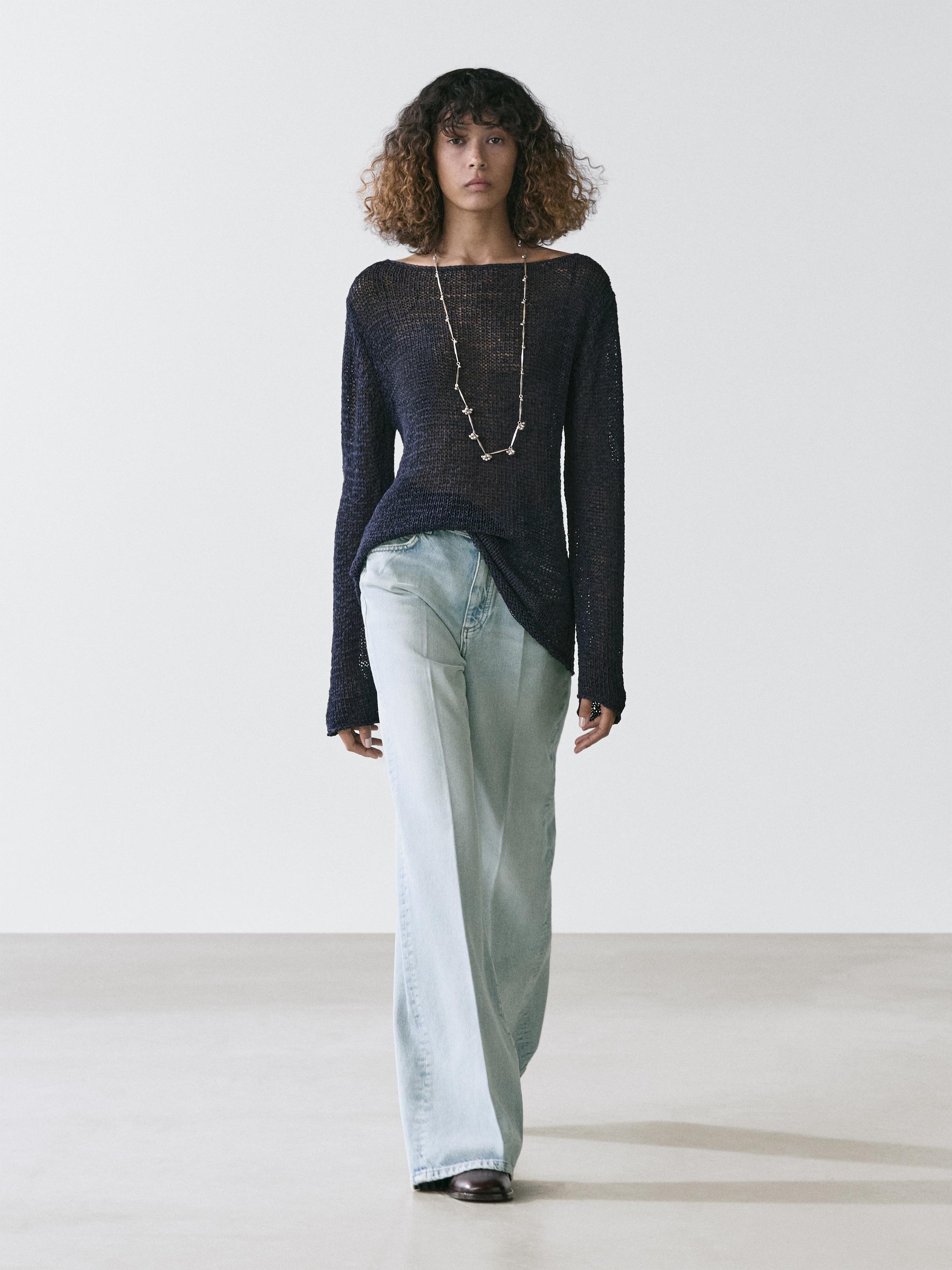 Conjunto de jeans palazzo azul claro y suéter negro de manga larga con collar largo.