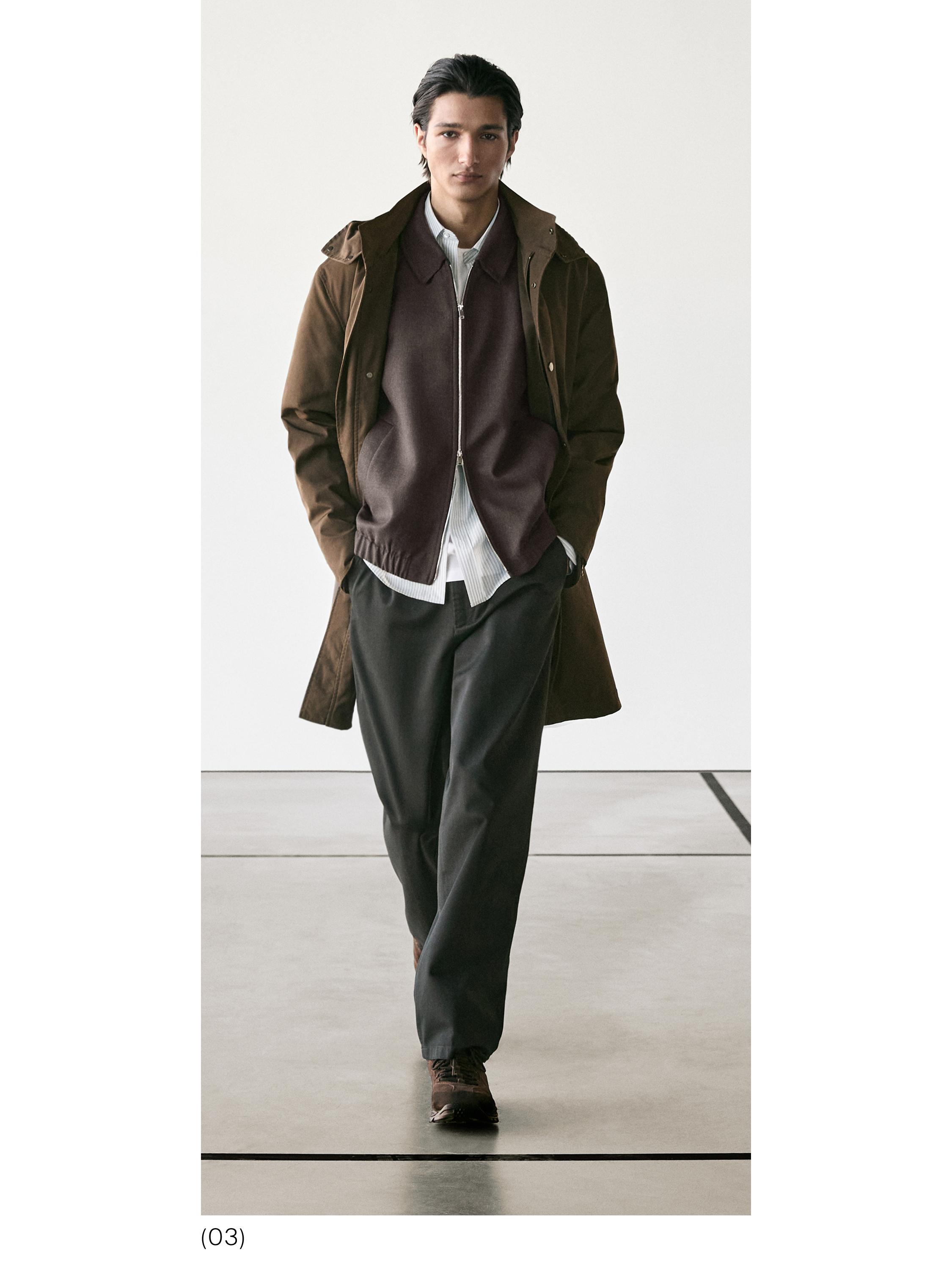 Brūns mētelis, jaka ar rāvējslēdzēju, balts krekls un tumšas bikses.