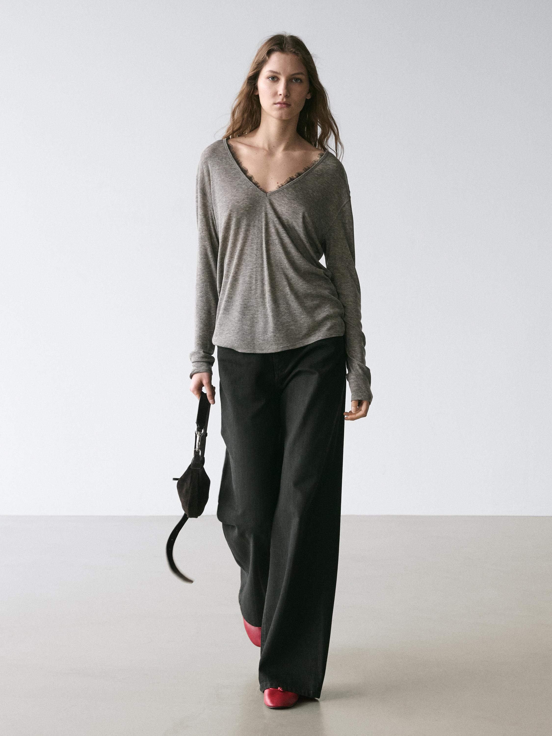 طقم يتكون من تي شيرت رمادي فاتح بأكمام طويلة ورقبة على شكل حرف V وتفاصيل من الدانتيل، وبنطلون أسود واسع، وحذاء أحمر.