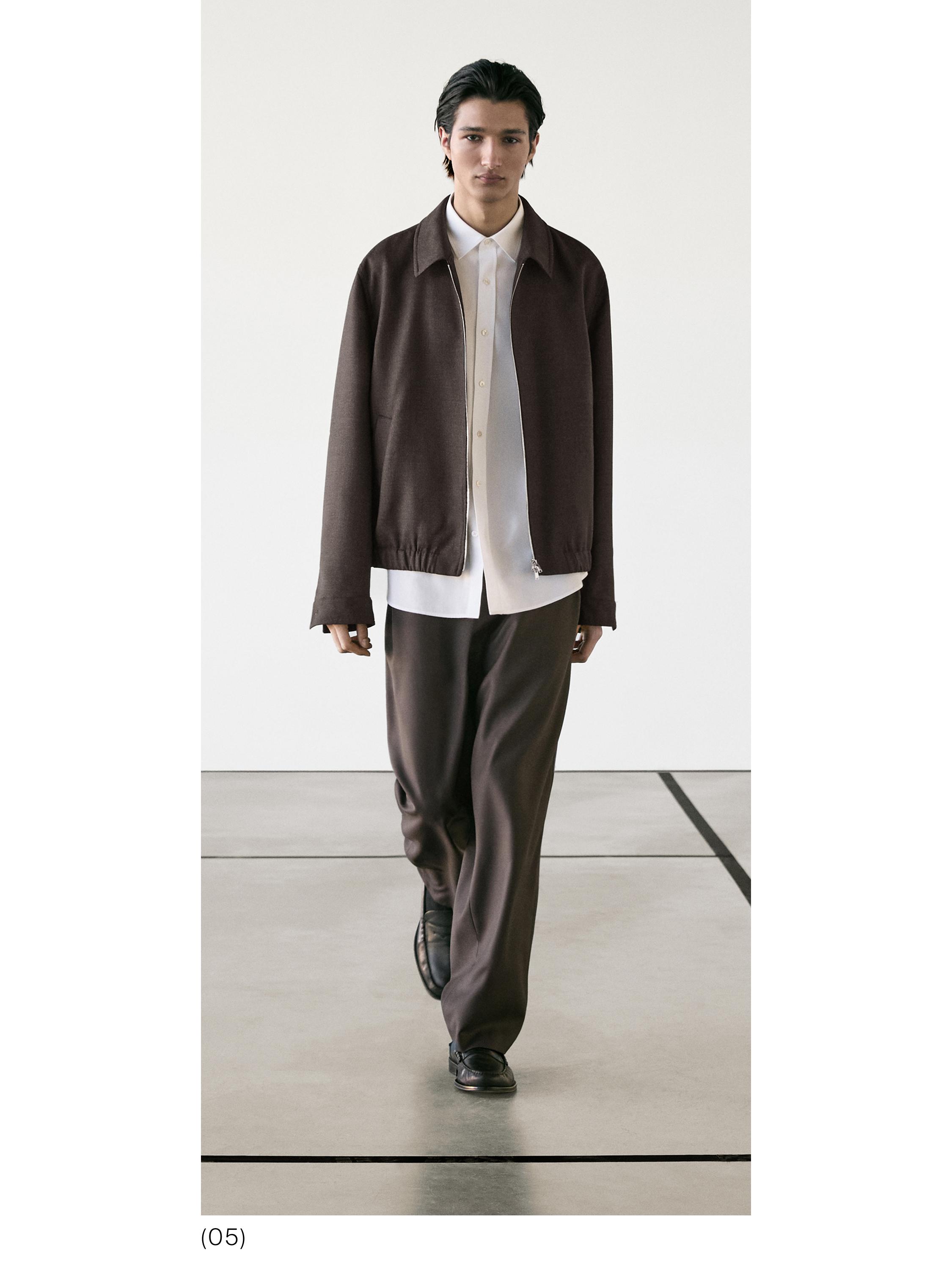 Brūns rāvējslēdzēja jakas komplekts, balts pogājams krekls un brūnas vaļīgas bikses.