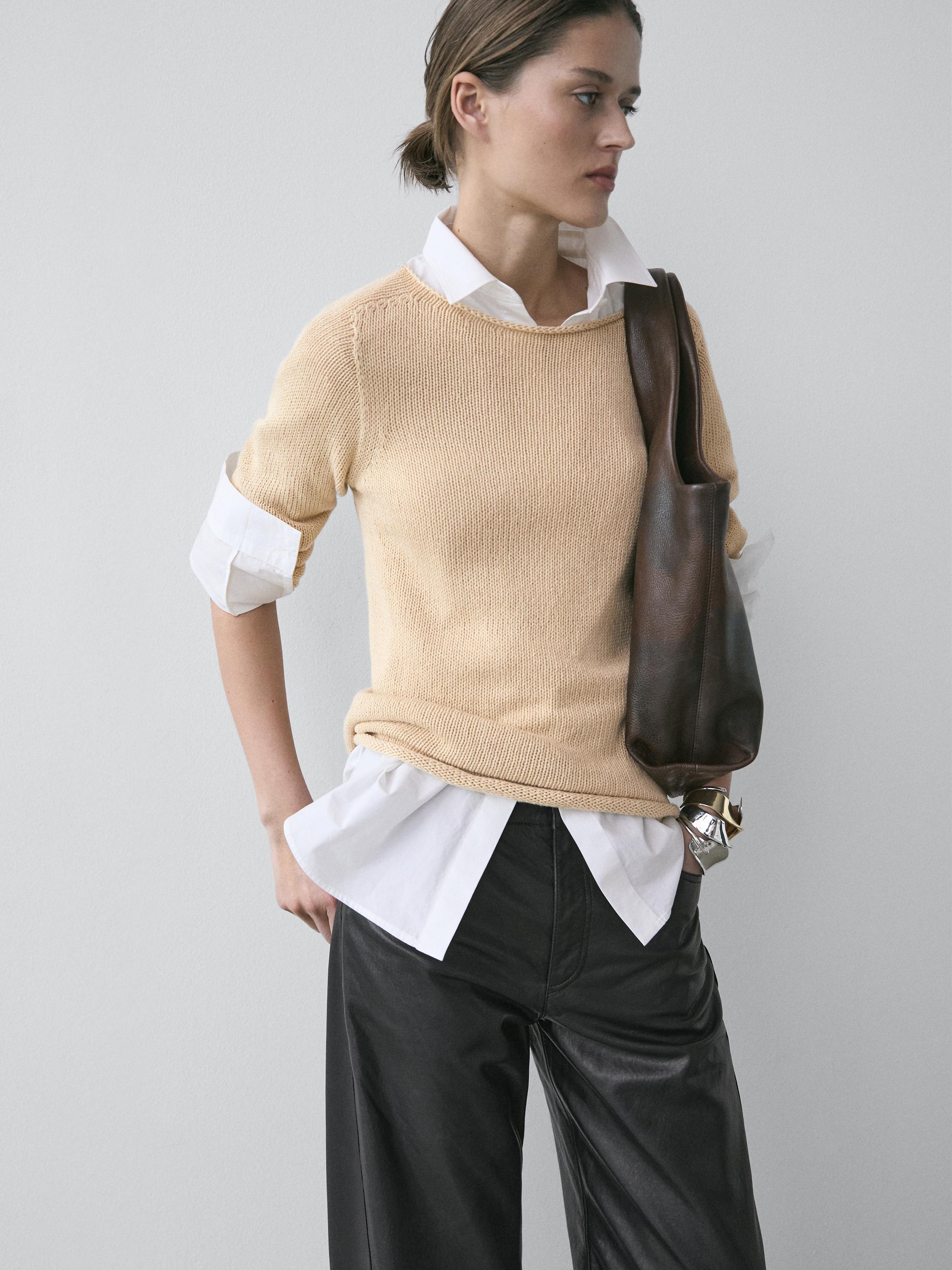 Conjunto de camisola de malha milho sobre camisa branca com calças pretas largas.