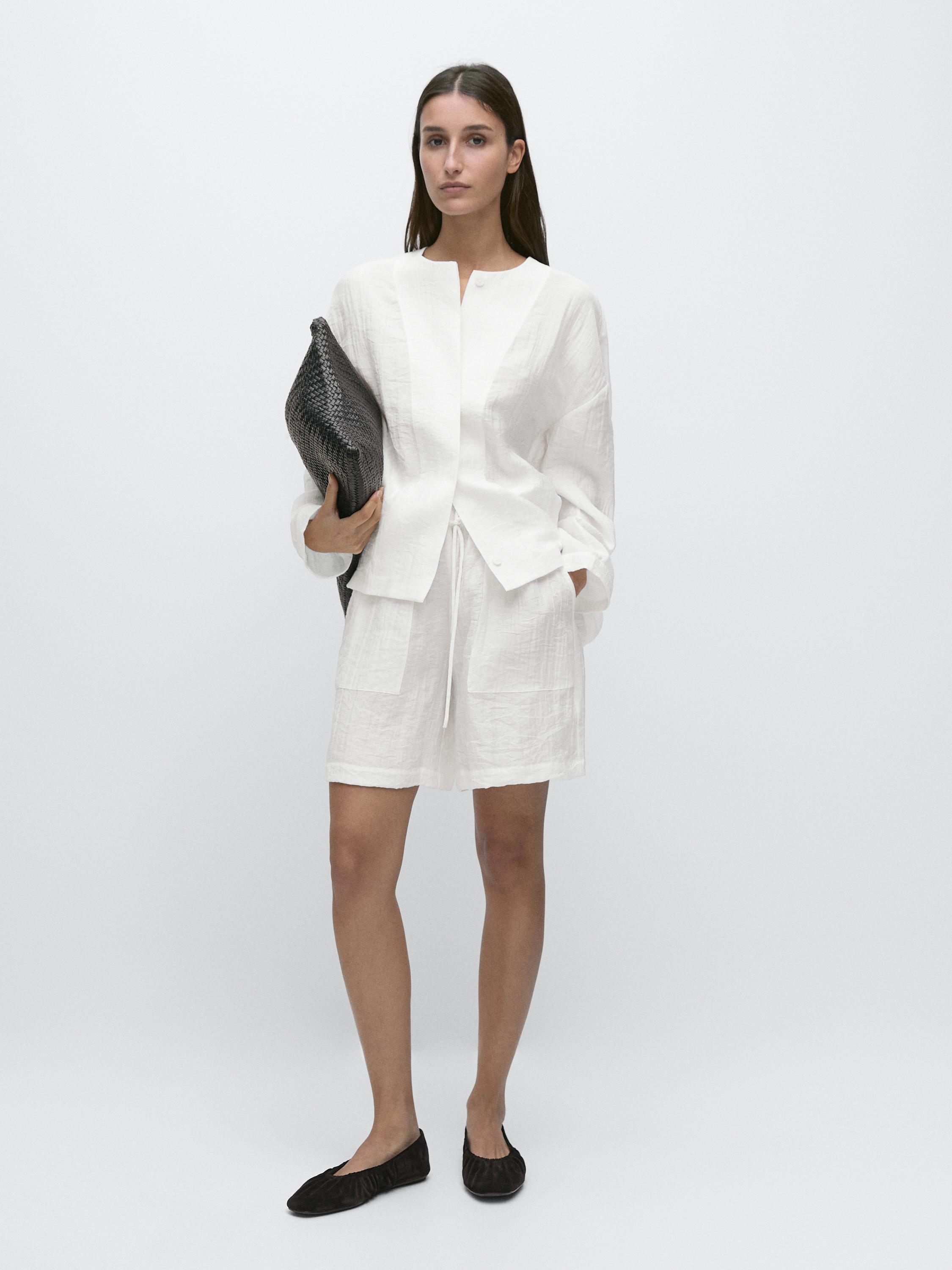 Conjunto de camisa blanca de manga larga y bermudas con bolsillos frontales, acompañado de zapatos negros.