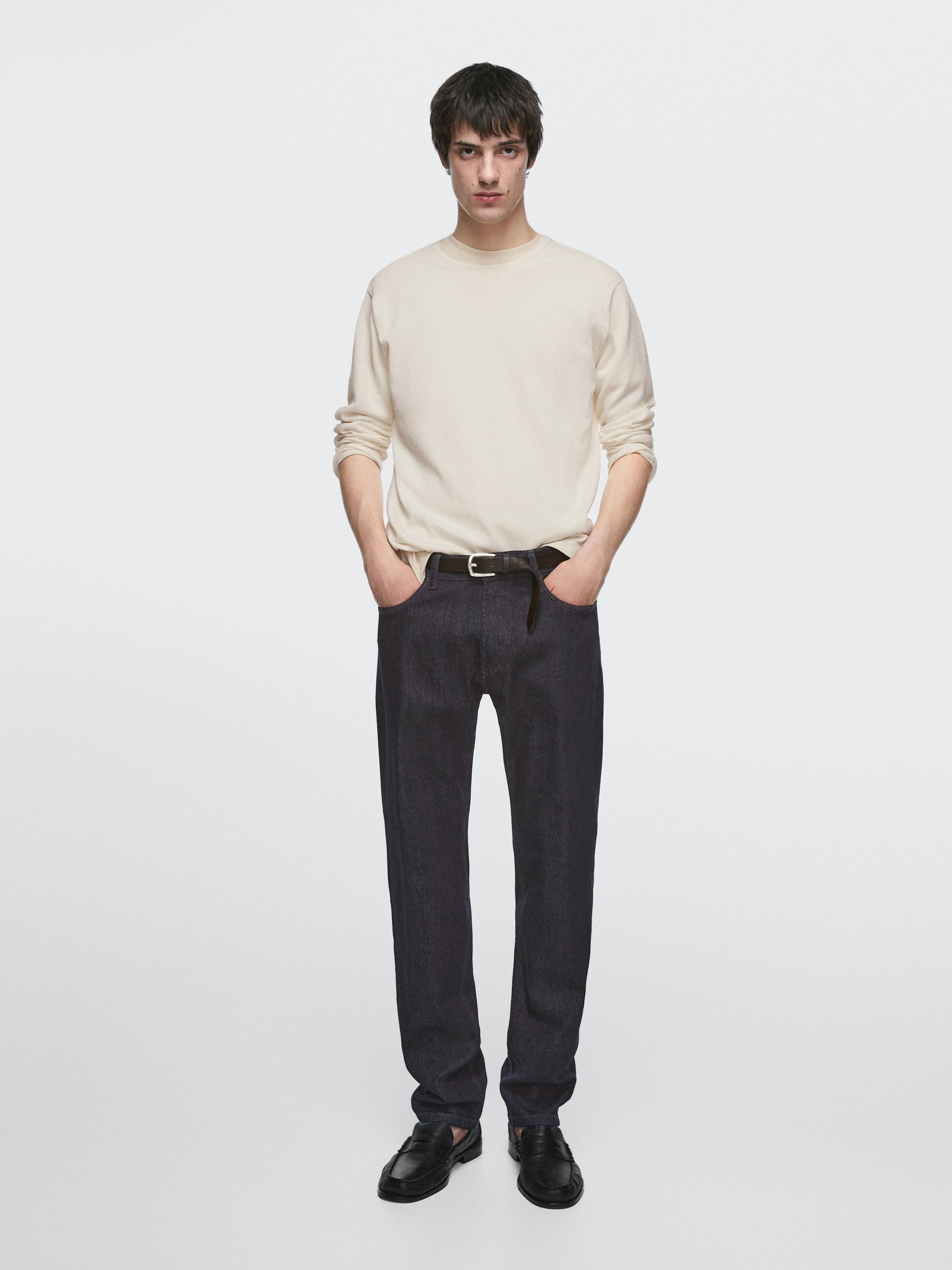 Ensemble jean slim fit bleu marine avec poches latérales et pull beige à manches longues.