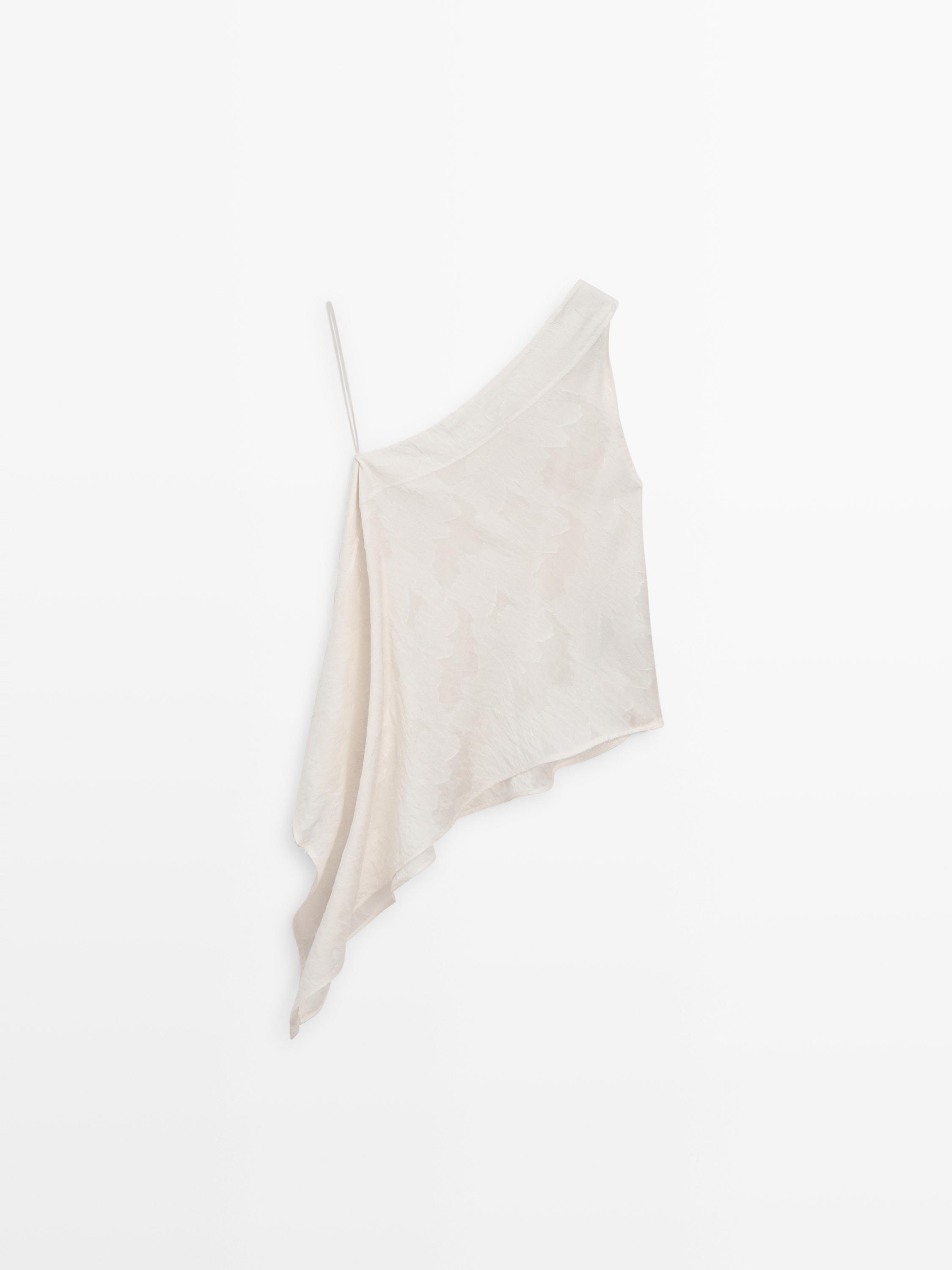 Μπροστινή όψη λευκού τοπ με ασύμμετρη λαιμόκοψη και λεπτή τιράντα. Ρευστός σχεδιασμός με πλάγια πτώση.