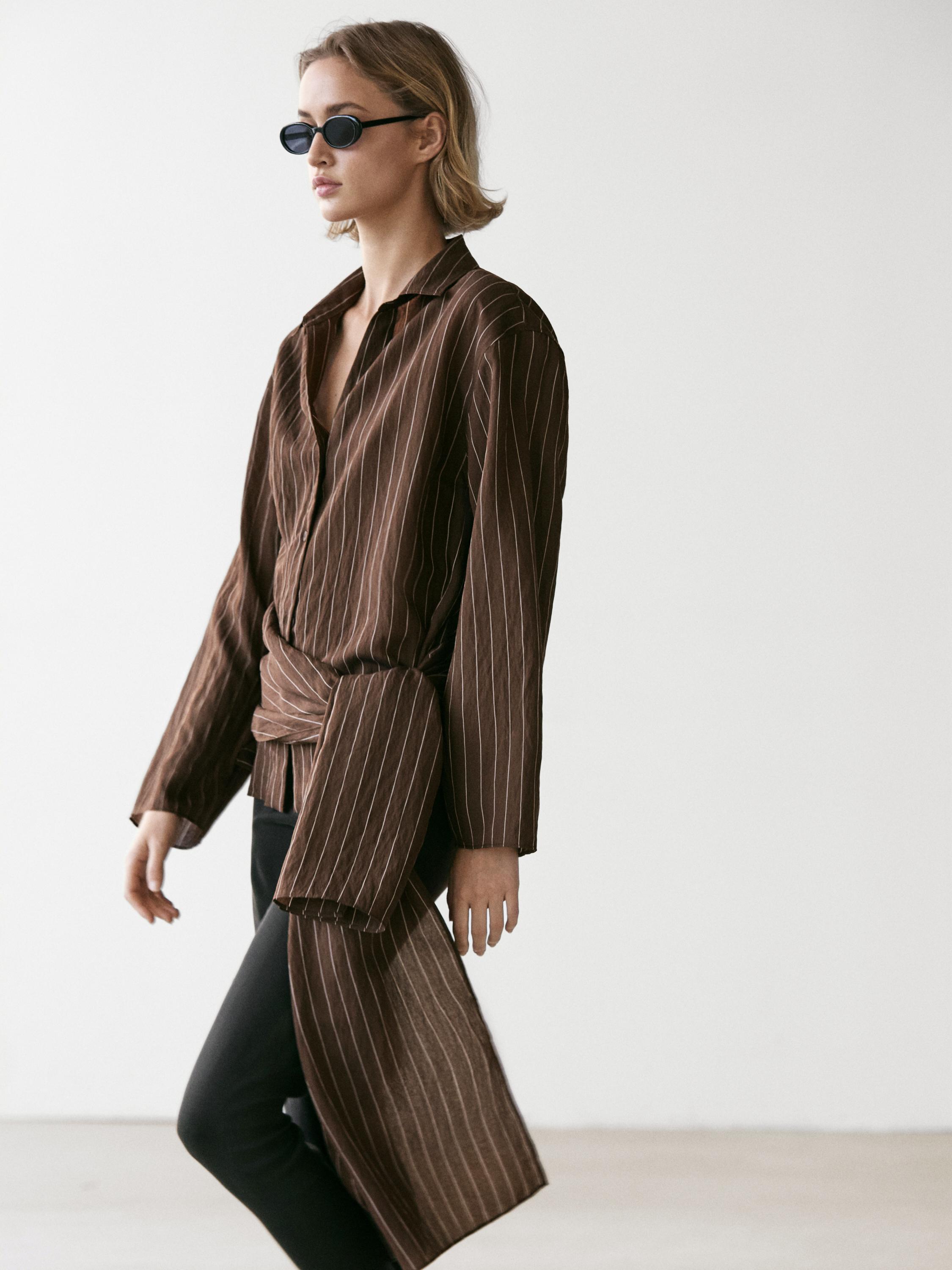 Conjunto de camisa café a rayas con detalle de pañuelo y pantalones negros.