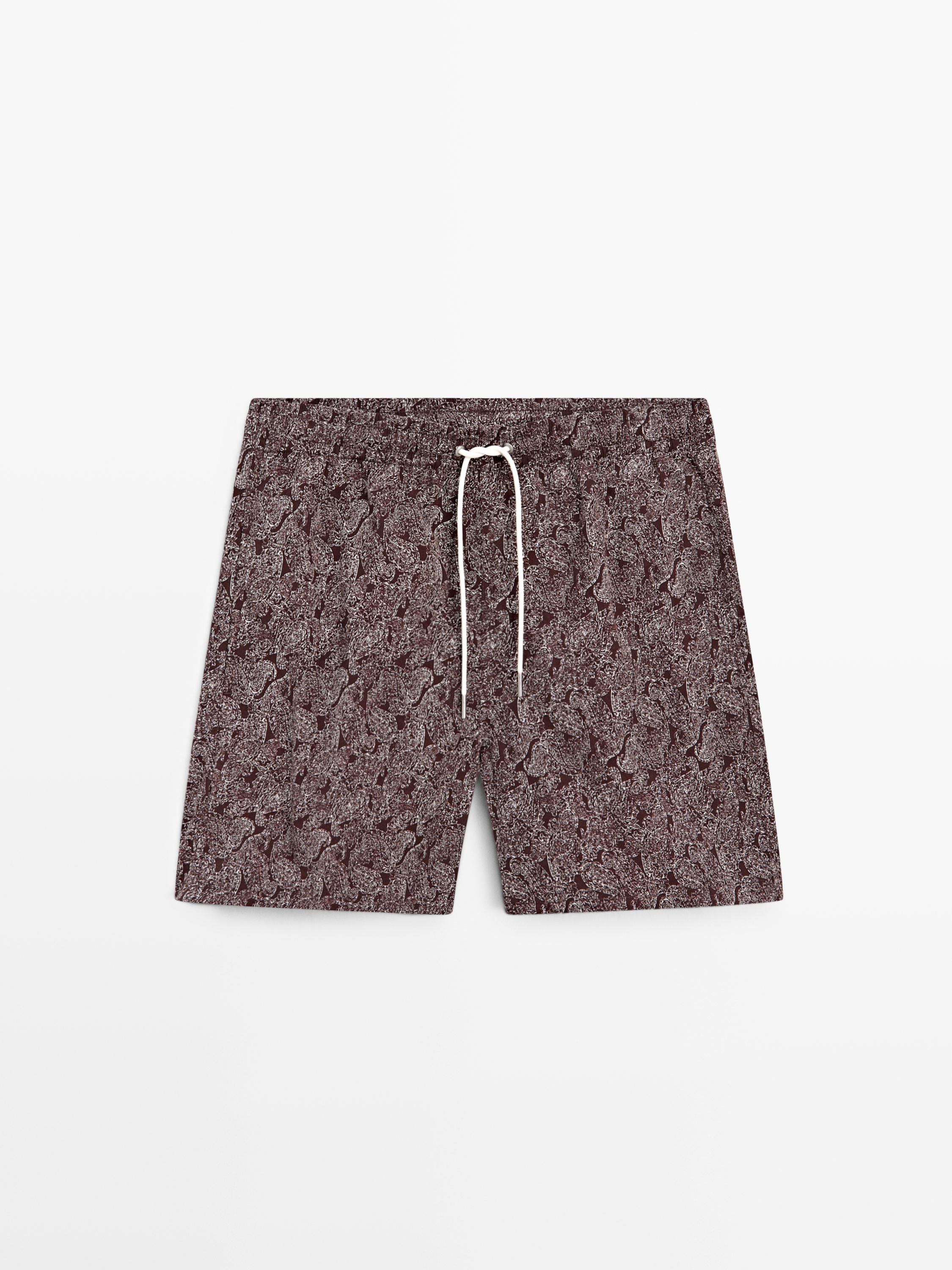 Vorderansicht eines lässigen, ziegelroten Badeanzugs mit abstraktem Muster und weißem Kordelzug an der Taille.