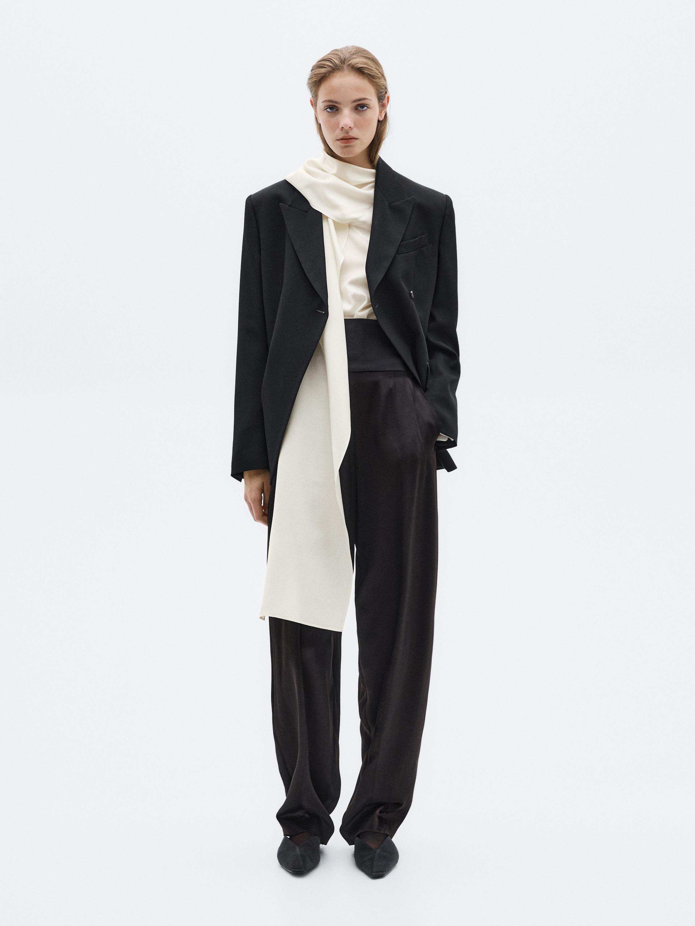 Set aus schwarzem Blazer, weißer Bluse mit langem Schal und lockerer schwarzer Hose.