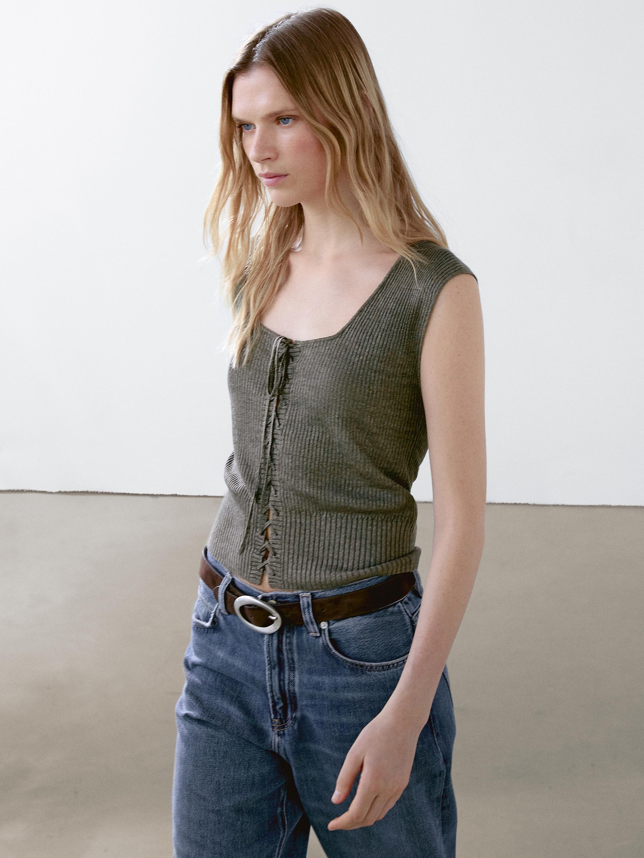 Ensemble composé d'un débardeur gris à col en V lacé, d'une ceinture marron et d'un jean bleu.