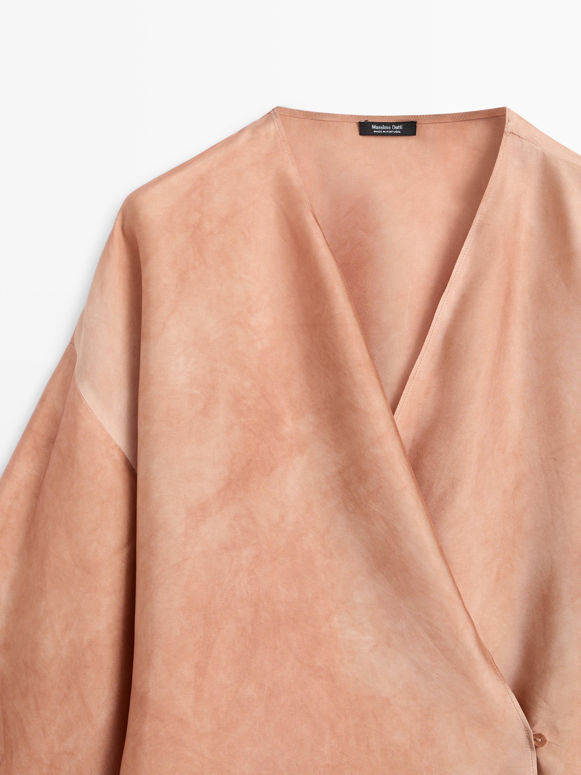 "Plano medio da parte superior dunha camisa beixe con colo en V e costuras visibles."