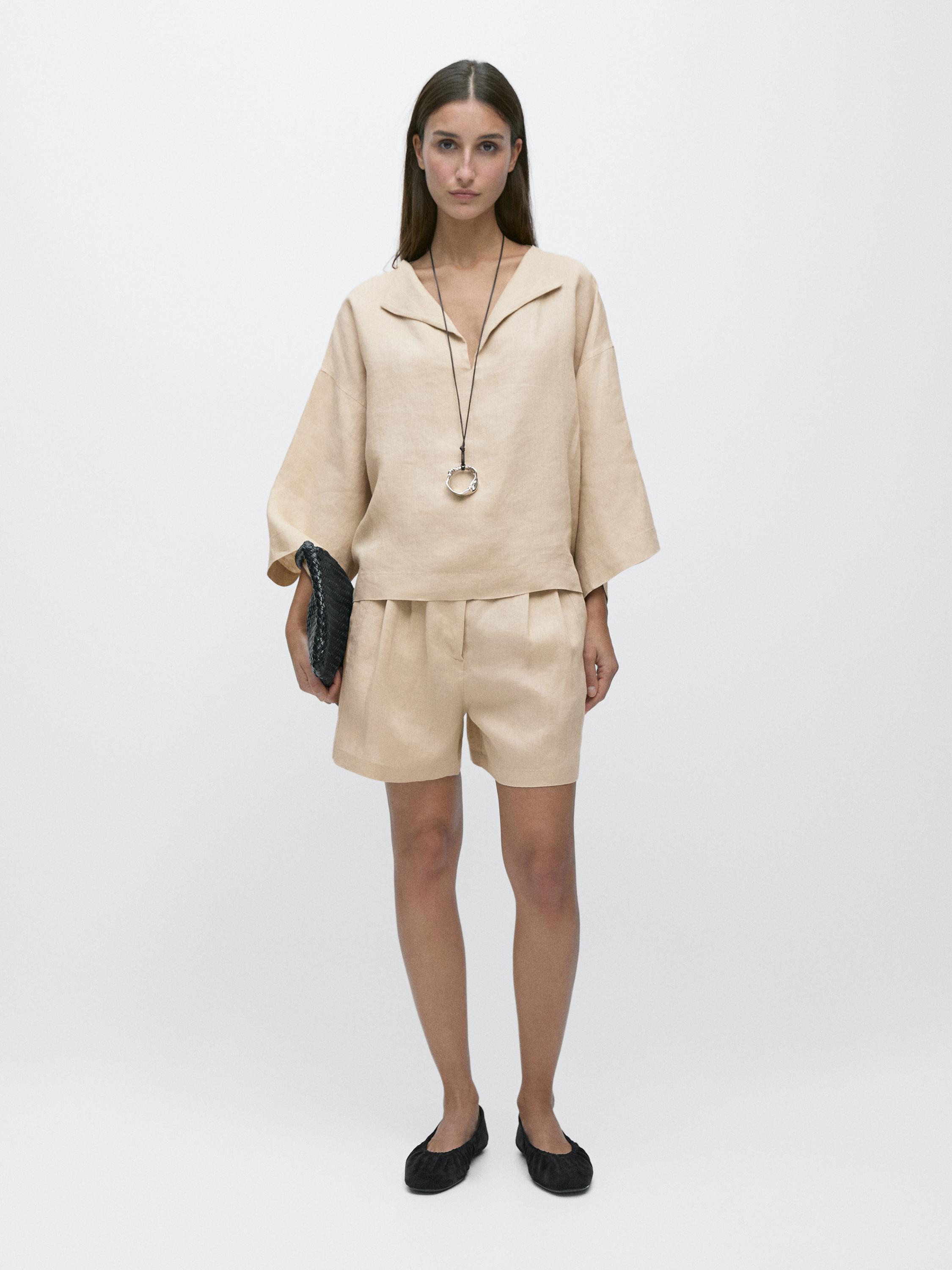 Flowy sand blouse set with an open collar and wide sleeves, matching pleated shorts, black bag, and flat shoes.