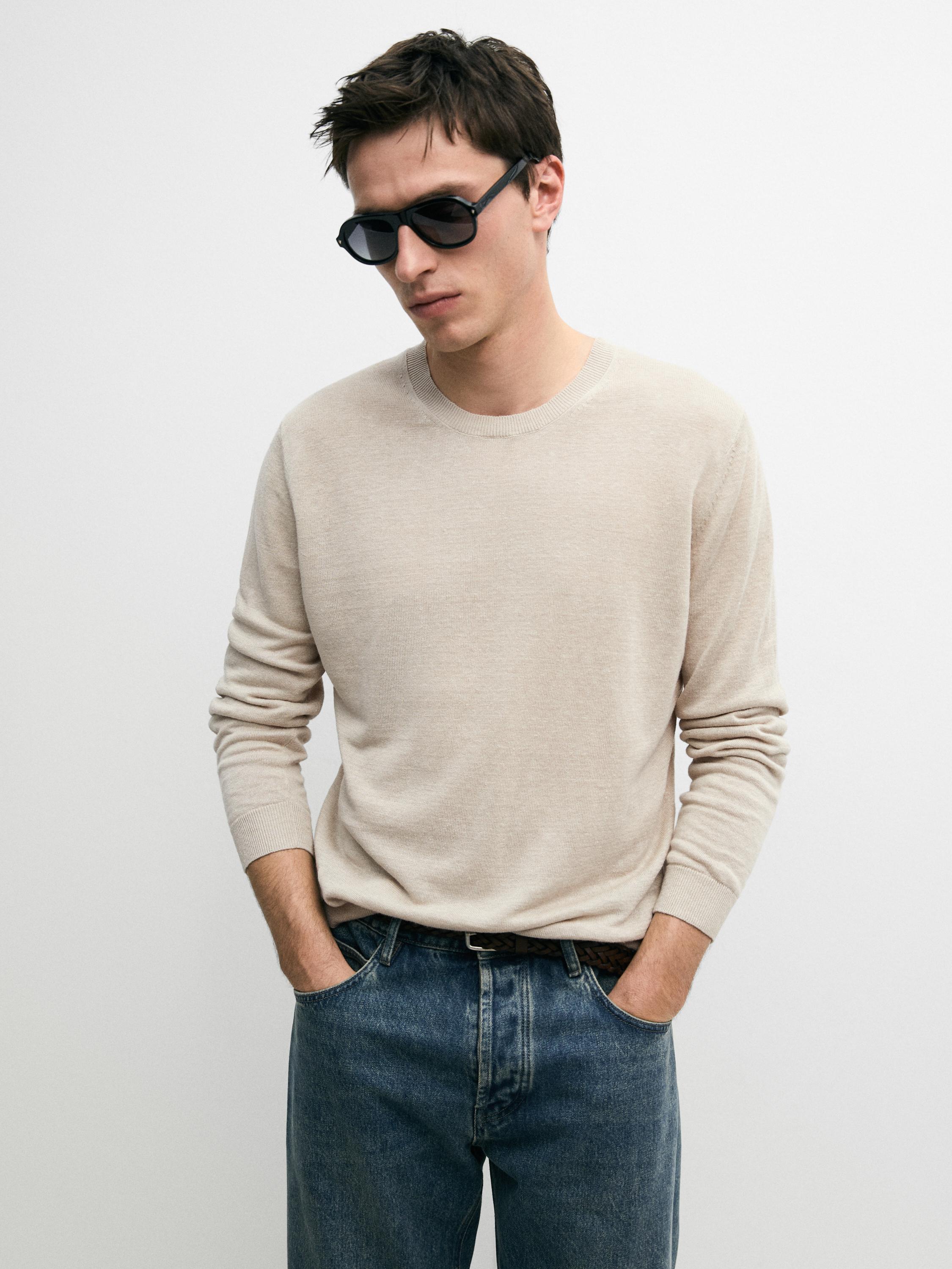 Beiges Strick-Jersey-Set mit Rundhalsausschnitt und blauen Jeans mit Fronttaschen.