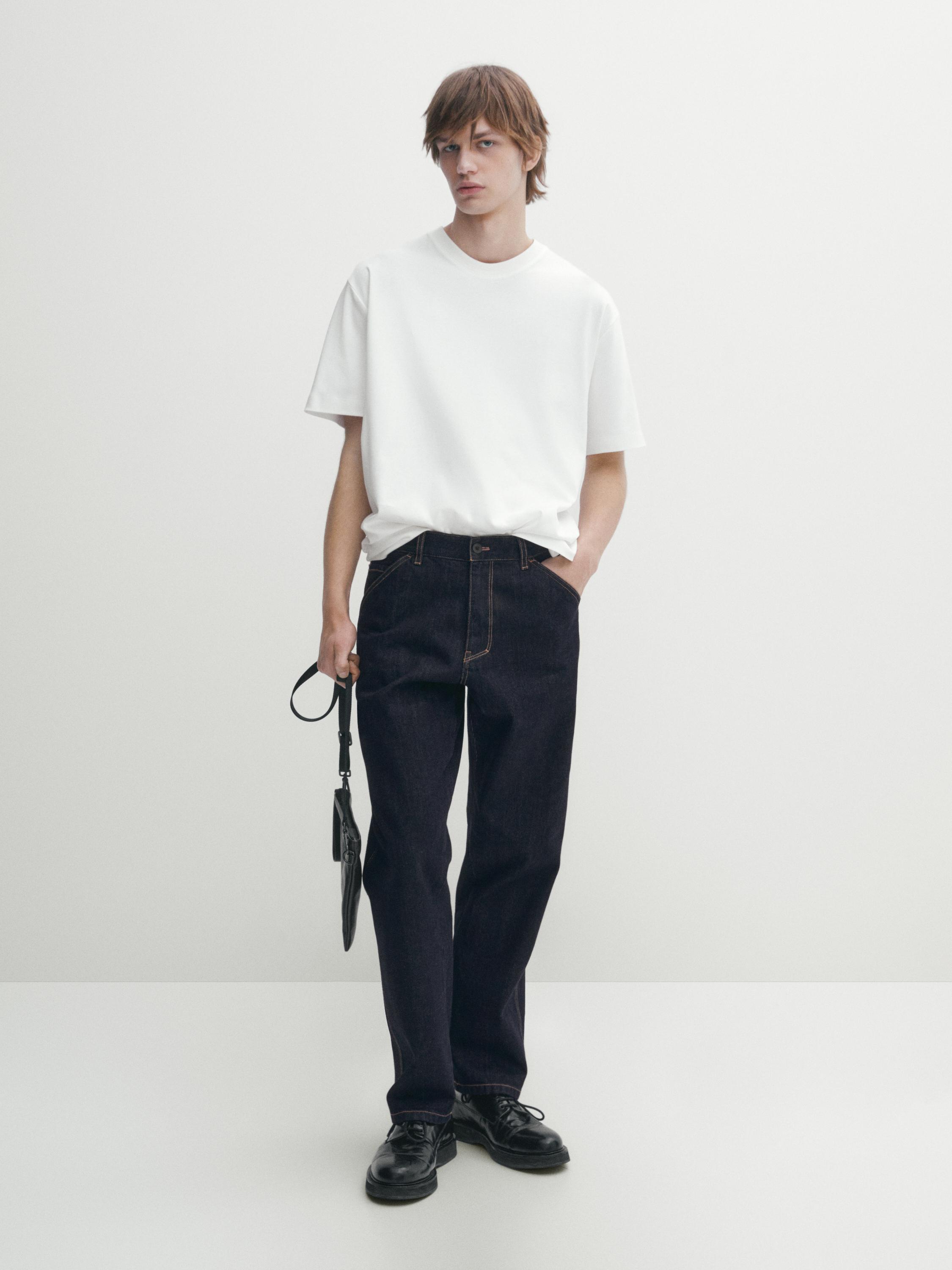 طقم يتكون من تي شيرت أبيض بأكمام قصيرة وياقة دائرية مع بنطلون جينز أزرق داكن وحذاء أسود.