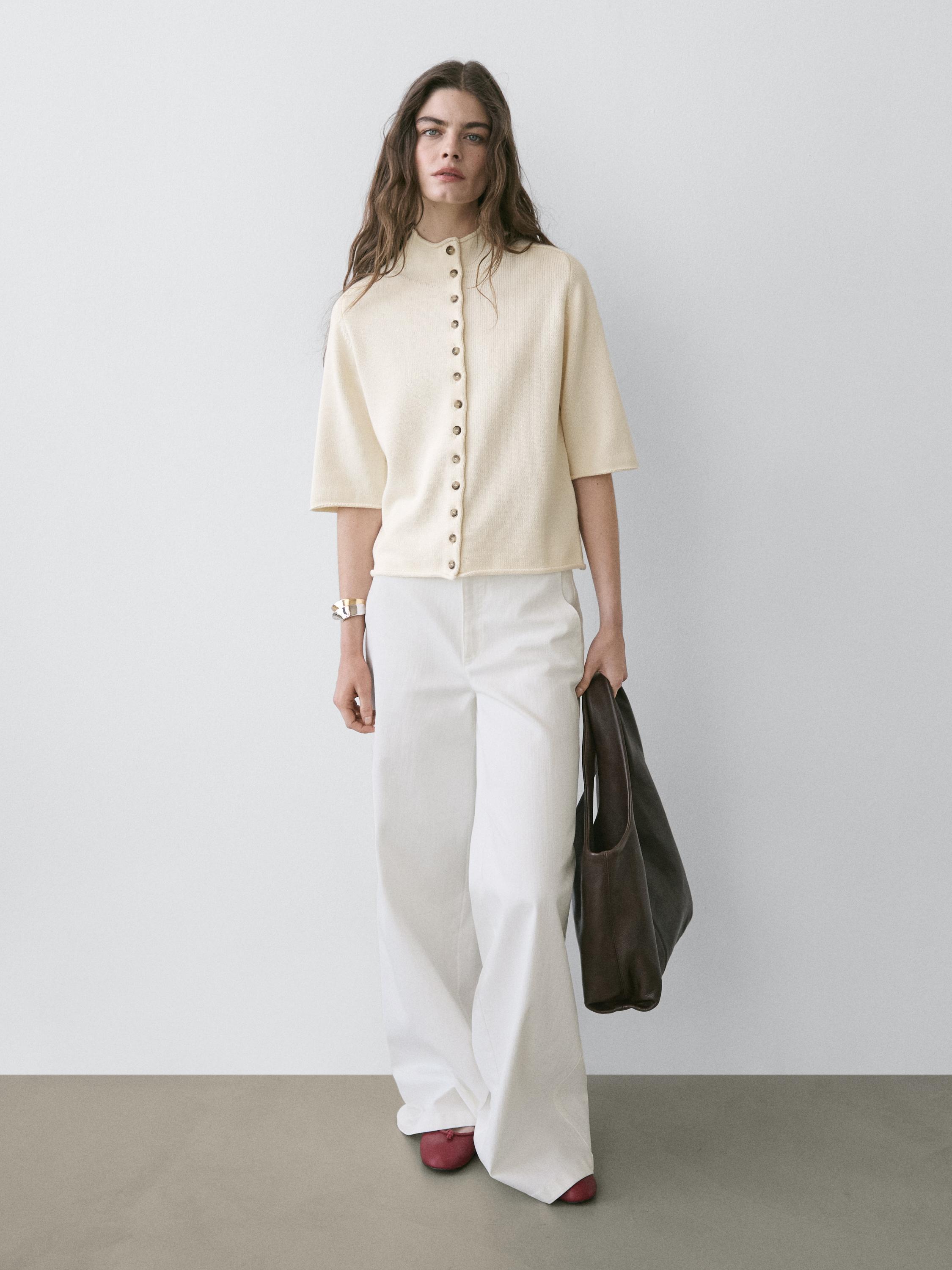 Crèmekleurige, kortmouwige vestset met knopen aan de voorkant en een wijde witte broek.