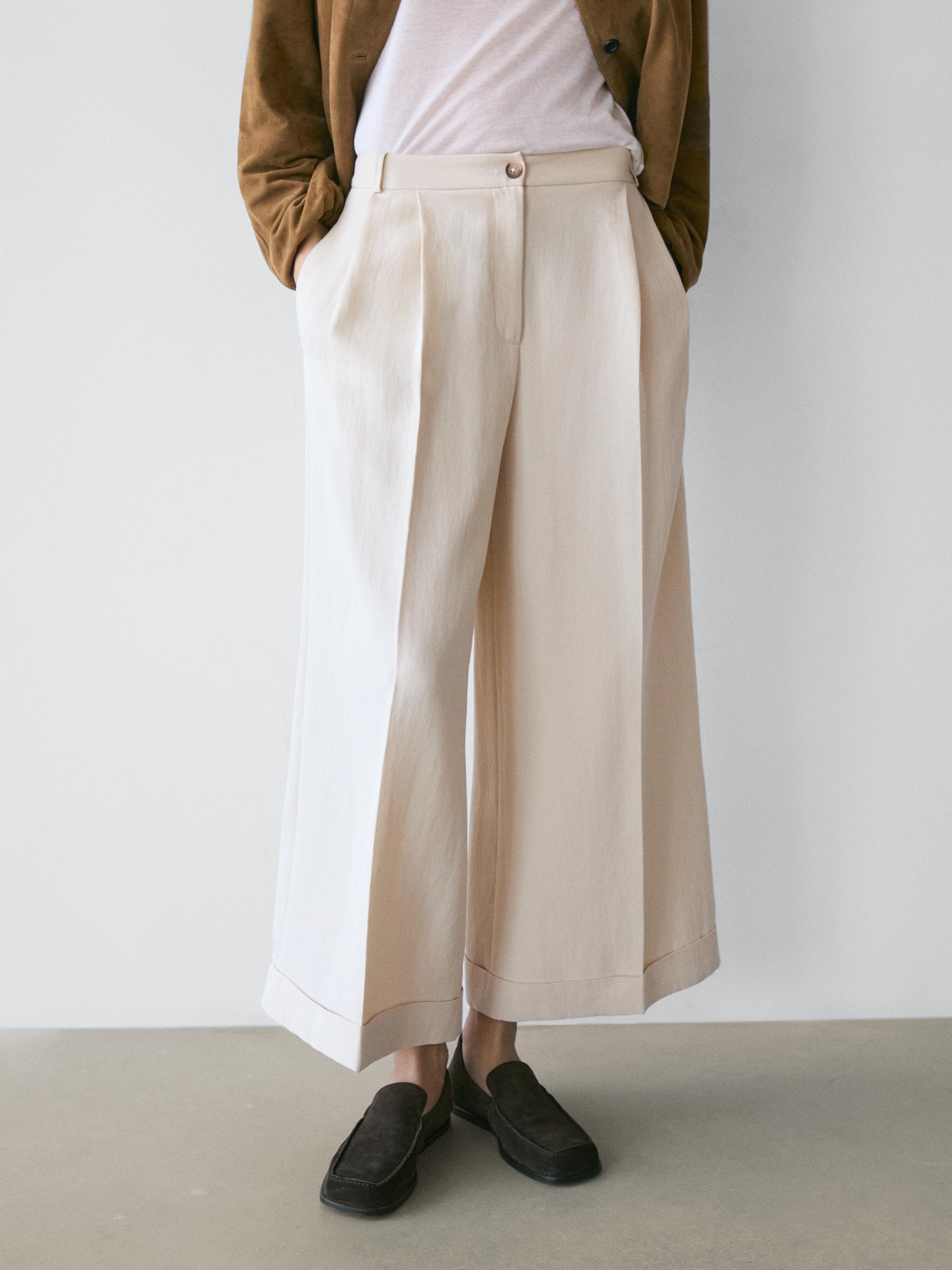 Mid-shot of fluid ecru pants with a turned-up hem, side pockets, and front pleats.