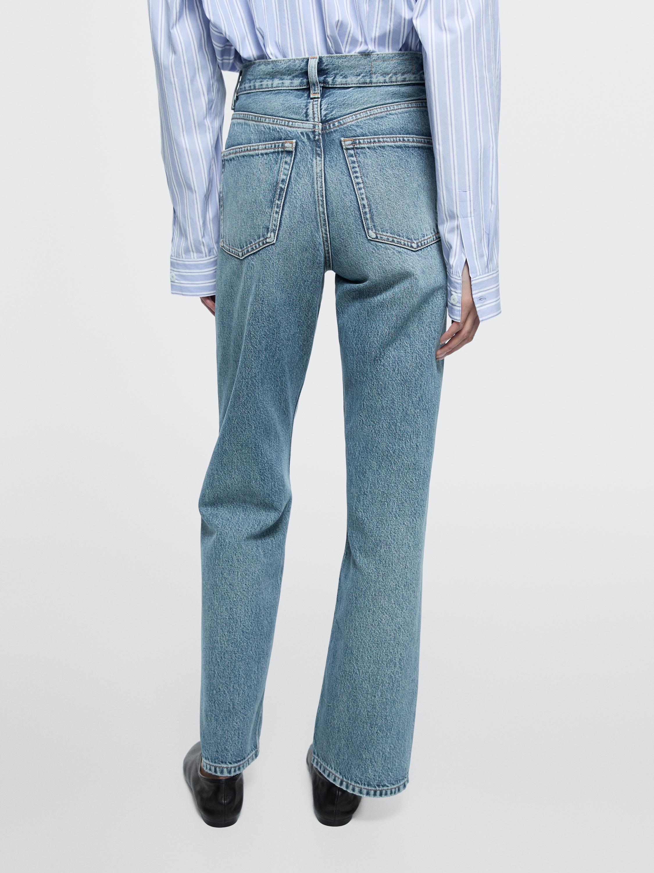 Conxunto de jeans azul claro de tiro alto con petos traseiros e camisa de raias verticais.