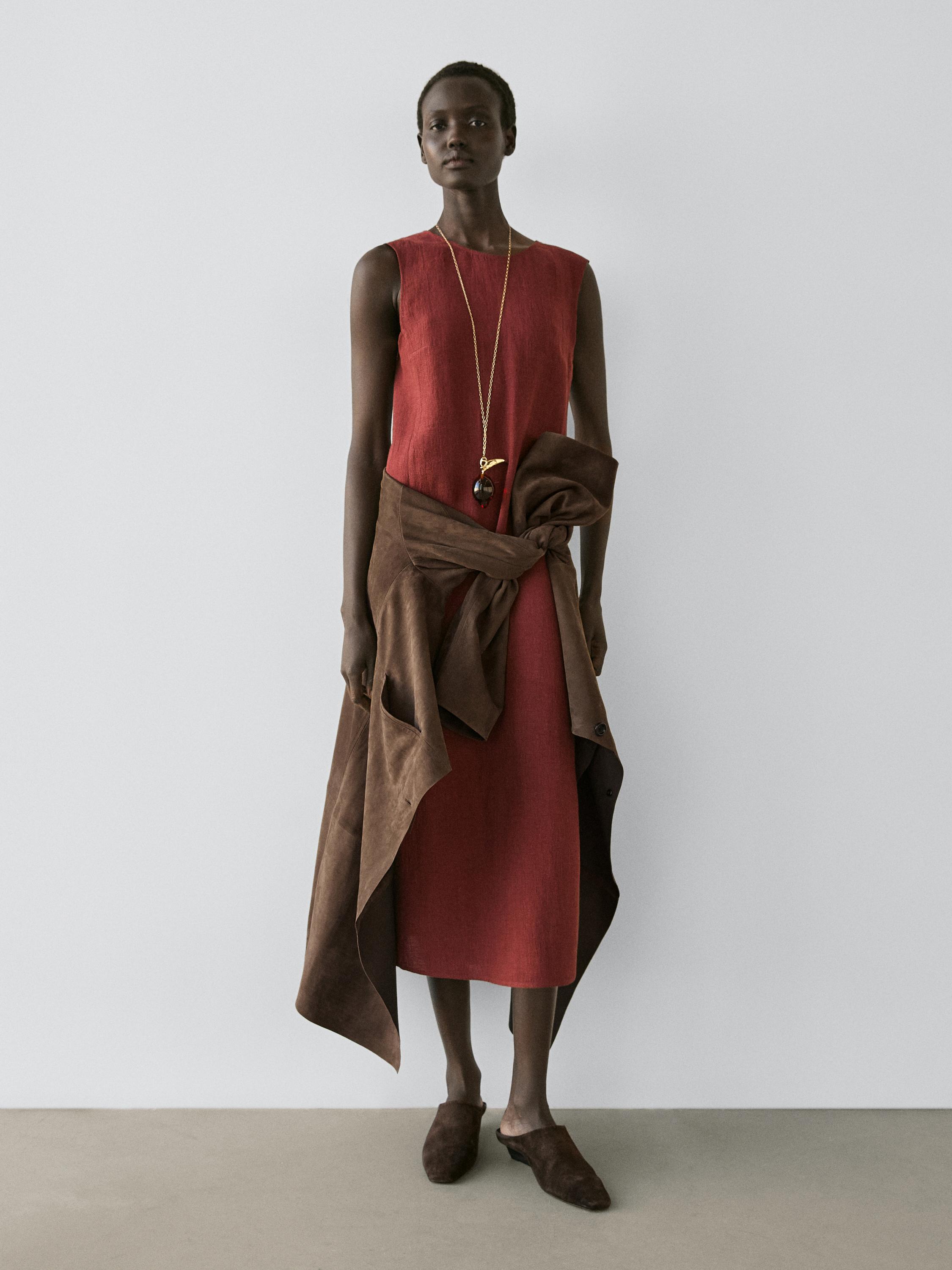 Rust sleeveless midi dress and brown jacket tied at the waist, with brown shoes.