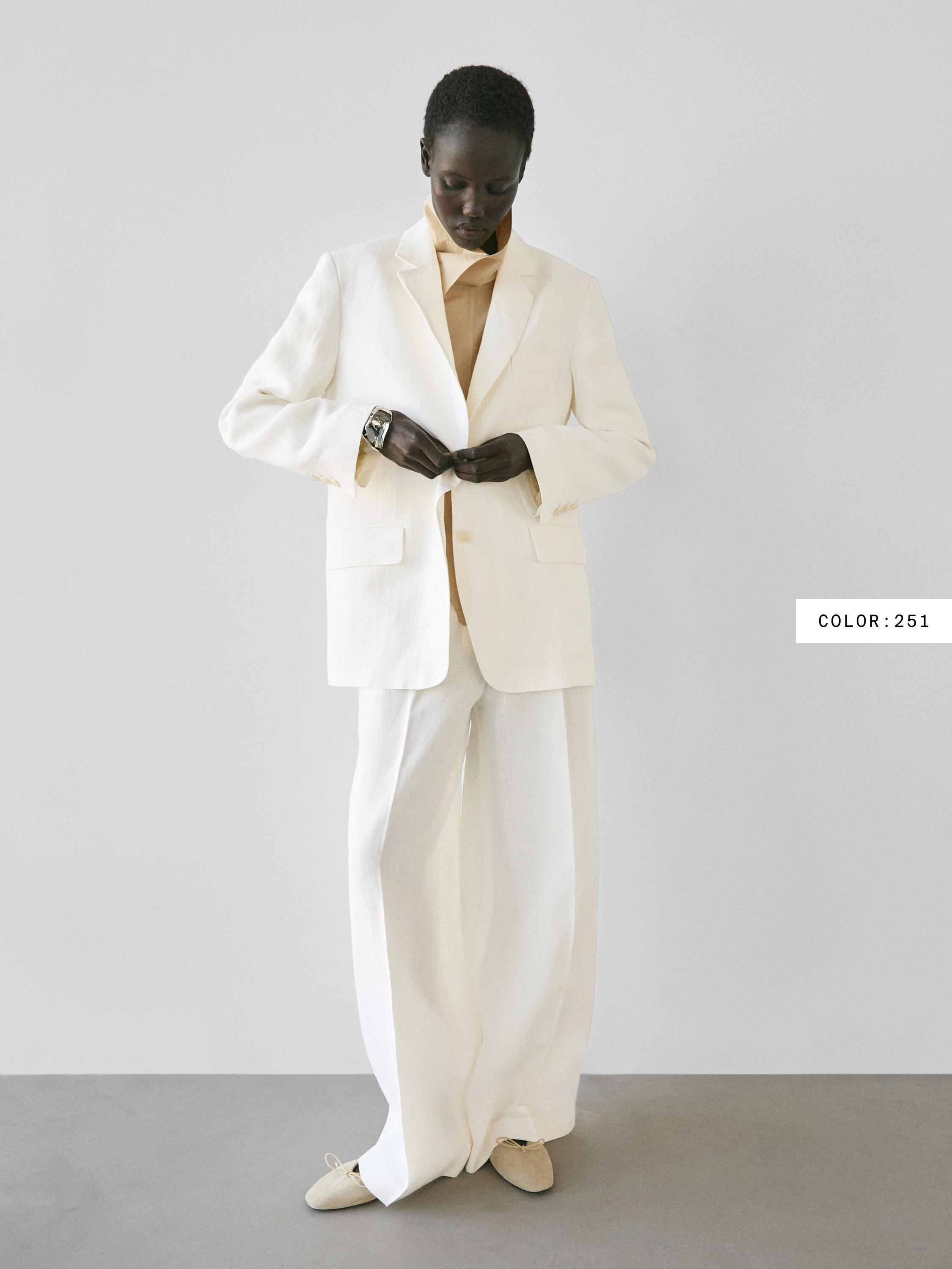 White suit set with a lapel jacket and front pockets, wide-leg pants, and a beige shirt.