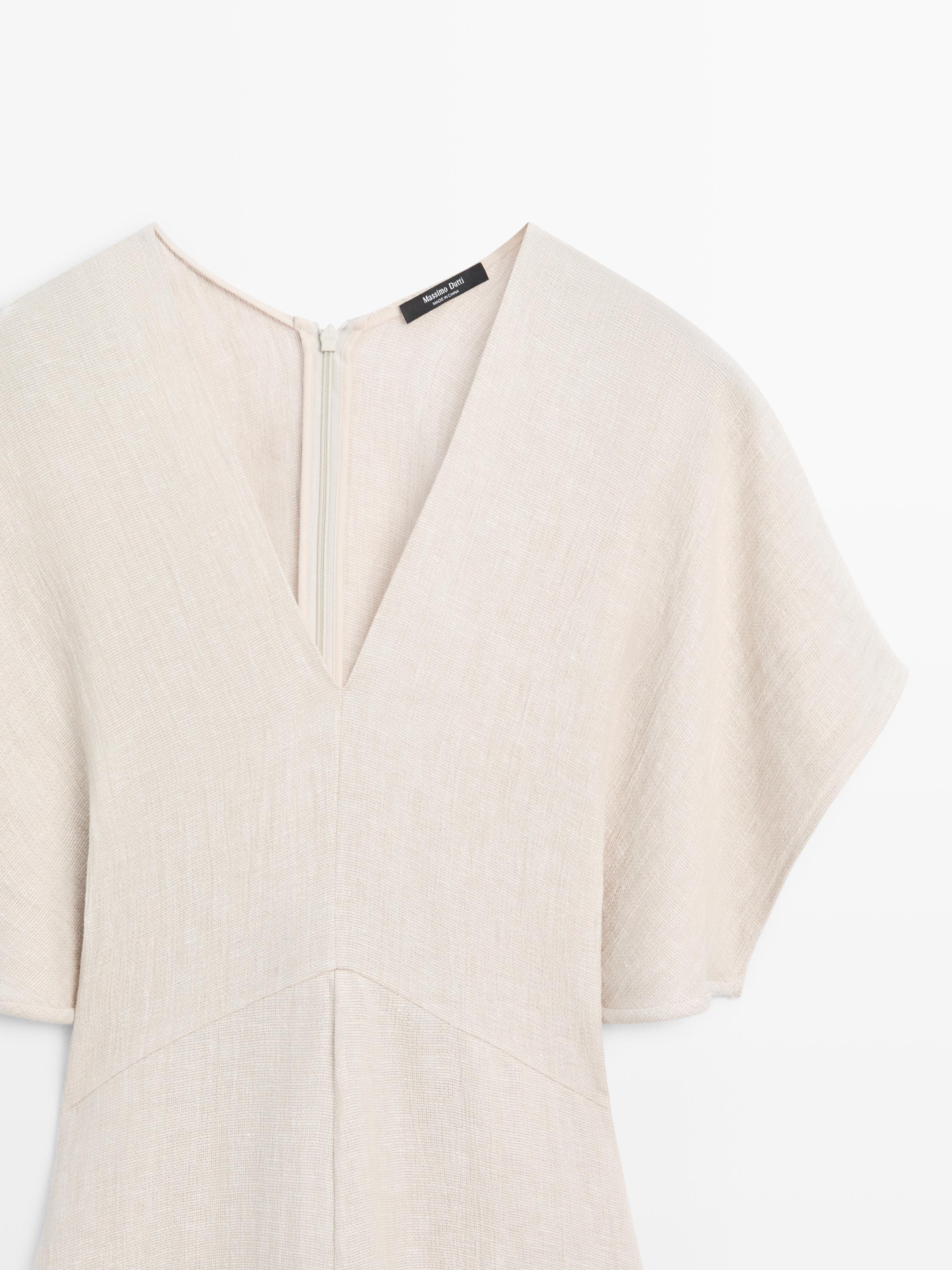 "V yakalı ve kısa kollu, ham renkli bir elbisenin üst kısmının detayı."