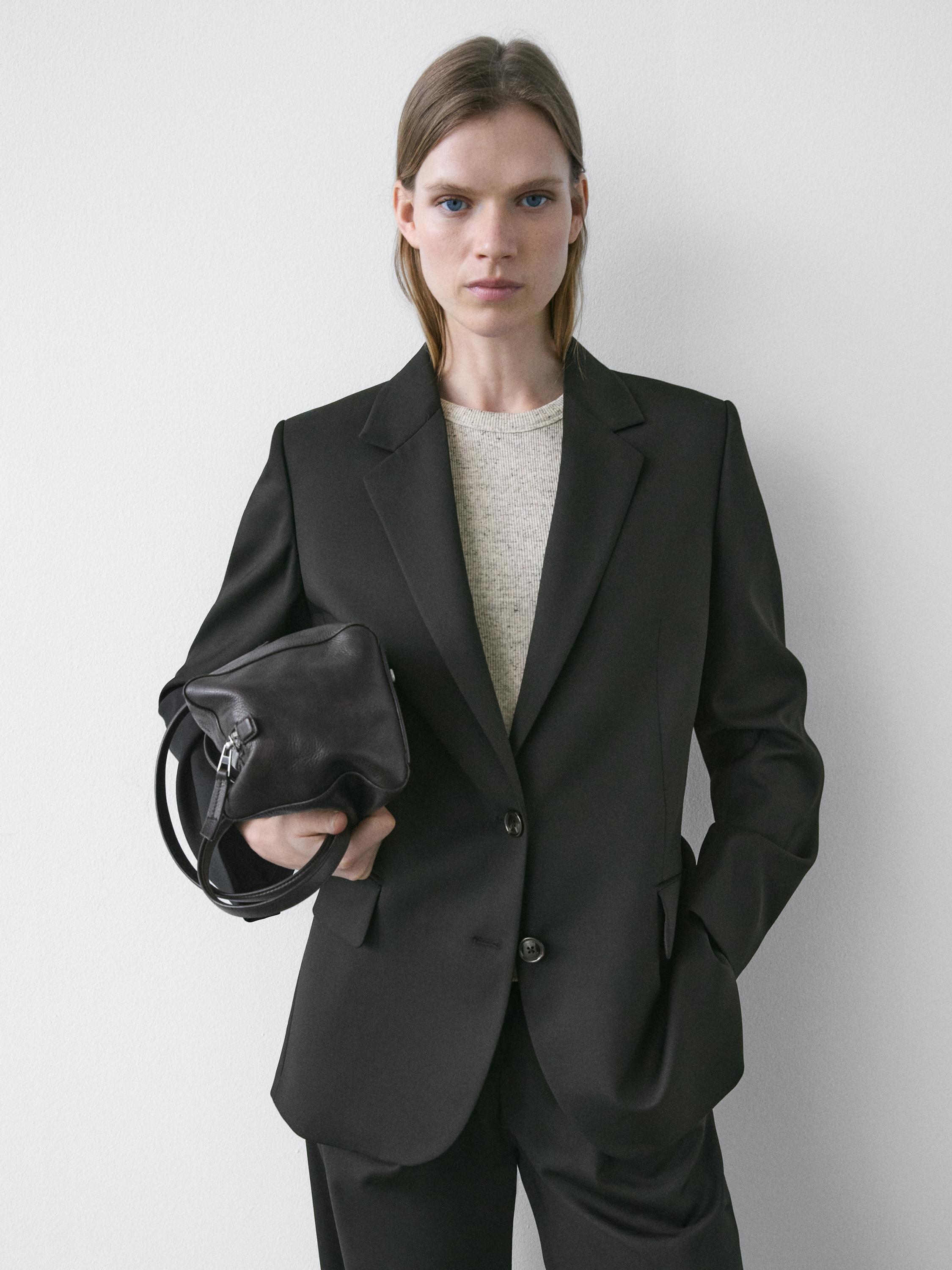Black blazer set with lapels and two buttons, light-colored T-shirt underneath, and matching pants. Visible side pockets.