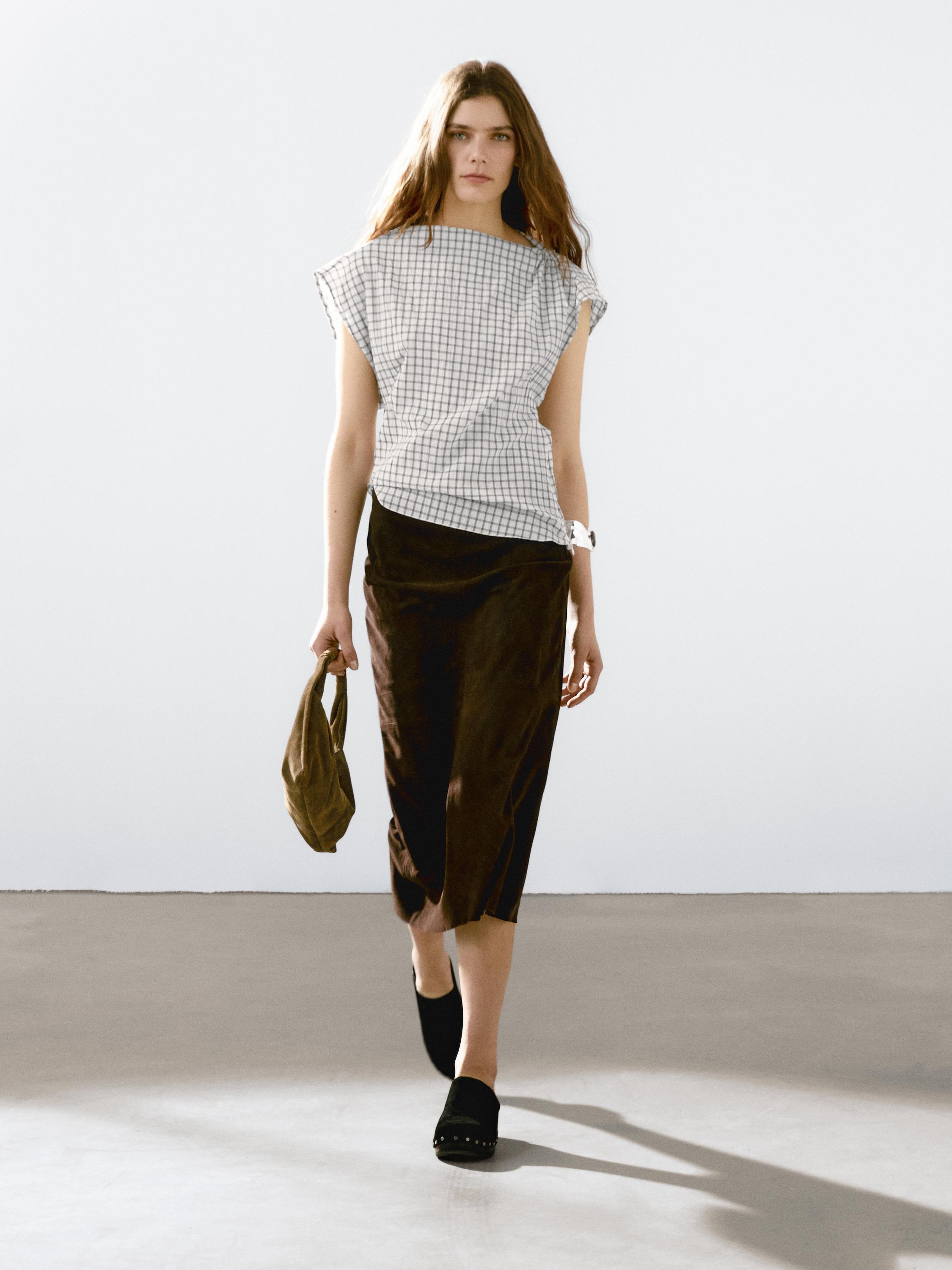Ensemble composé d'un chemisier à carreaux sans manches et d'une jupe marron mi-mollet, petit sac à main à la main