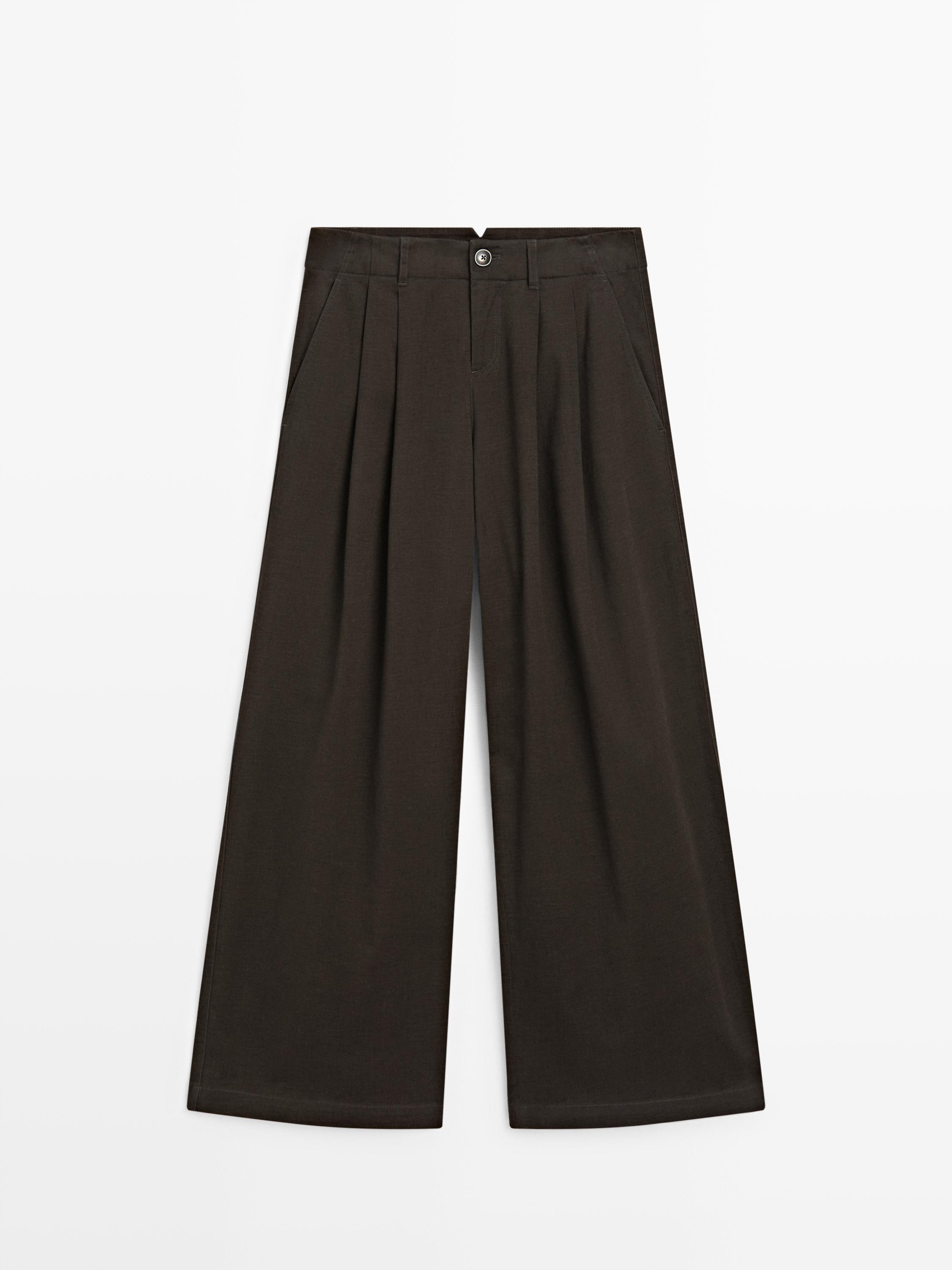 აქლემისფერი შარვლის წინა ხედი ნაკეცებით, ფართო ტოტებითა და გვერდითი ჯიბეებით. ღილაკითა და ელვაშესაკრავით.