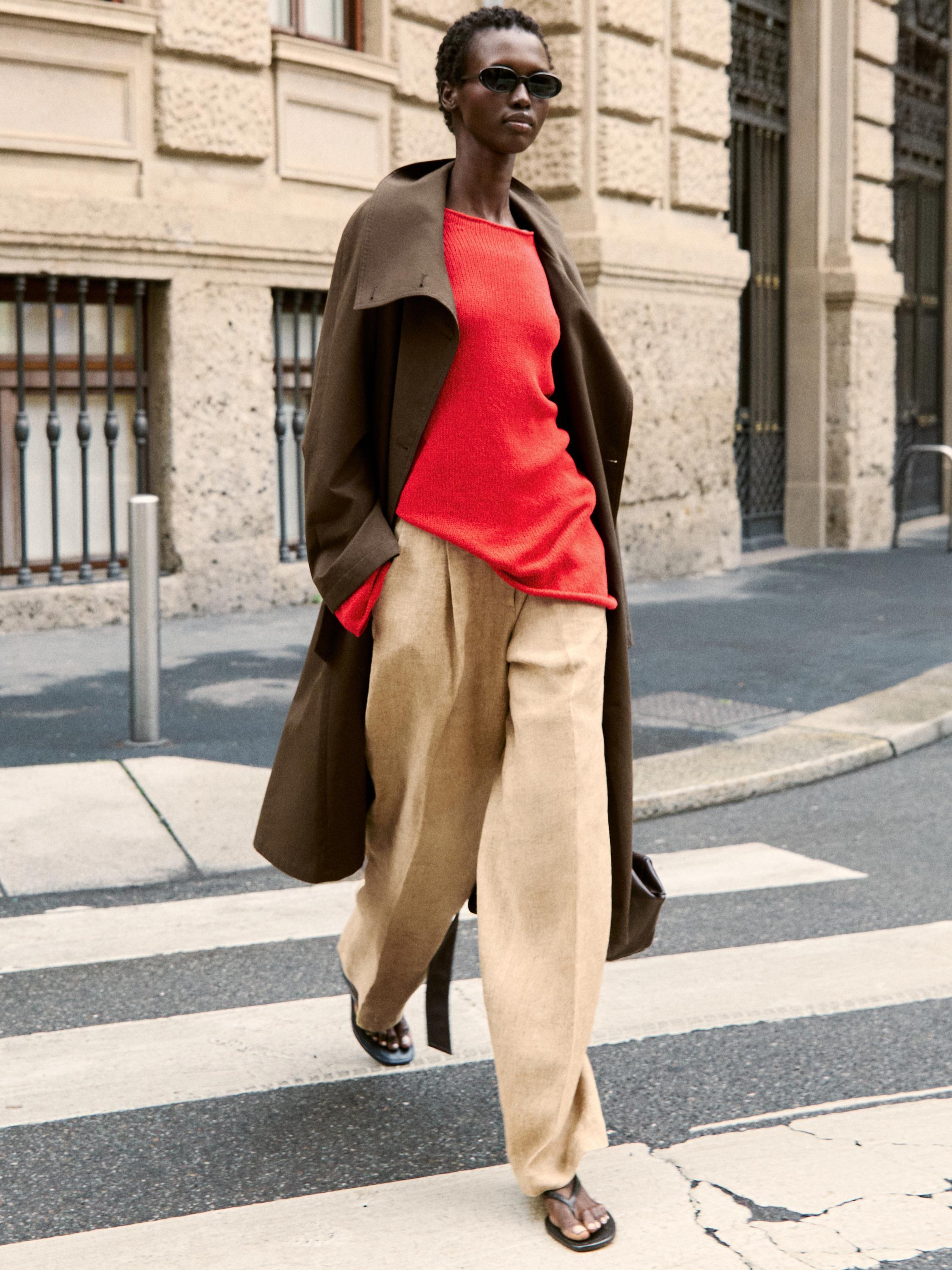 Ensemble avec manteau marron, pull rouge et pantalon large beige.
