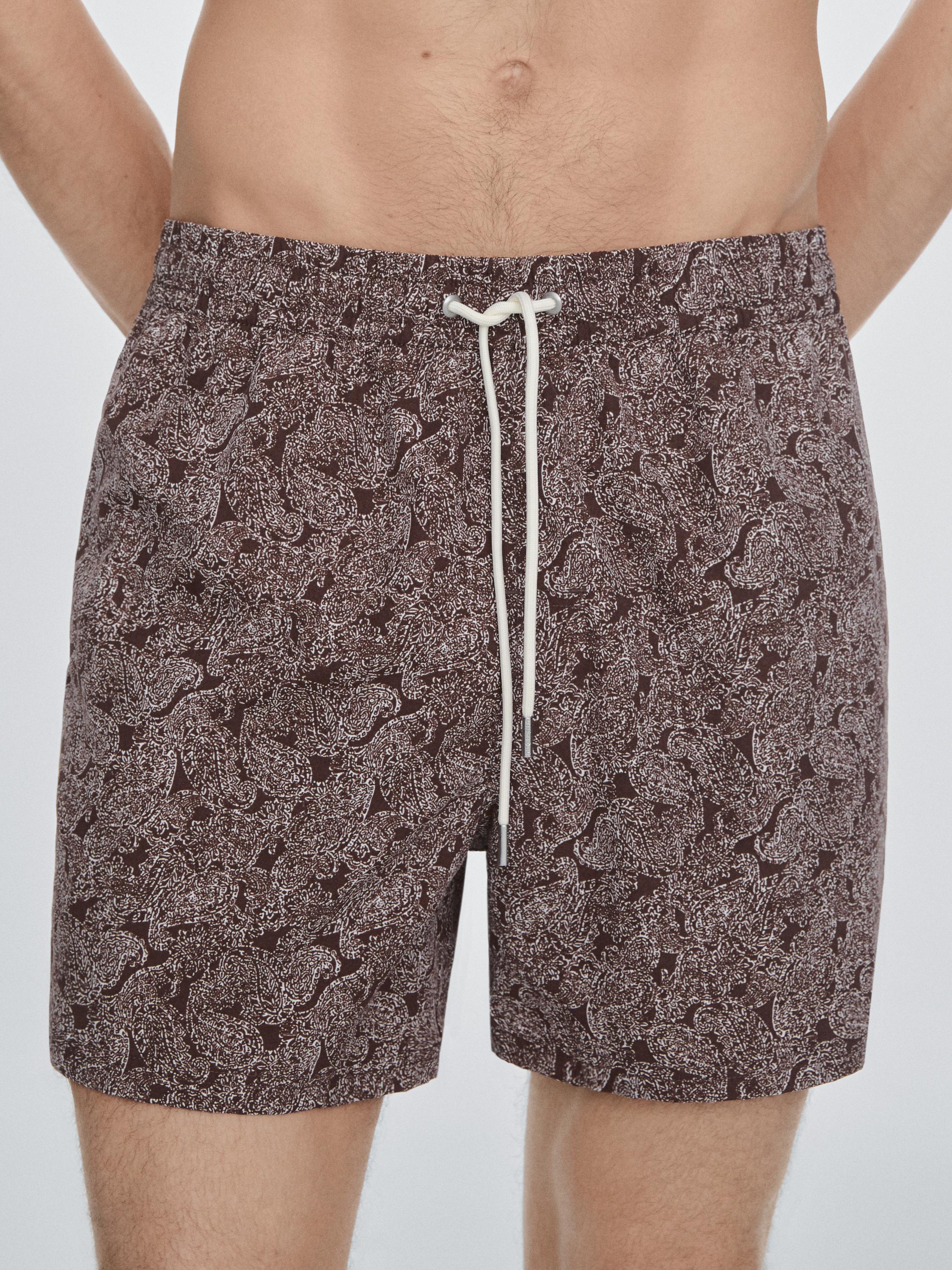 Halbnahe Aufnahme eines ziegelroten Badeanzugs mit Paisleymuster und weißem Kordelzug an der Taille.