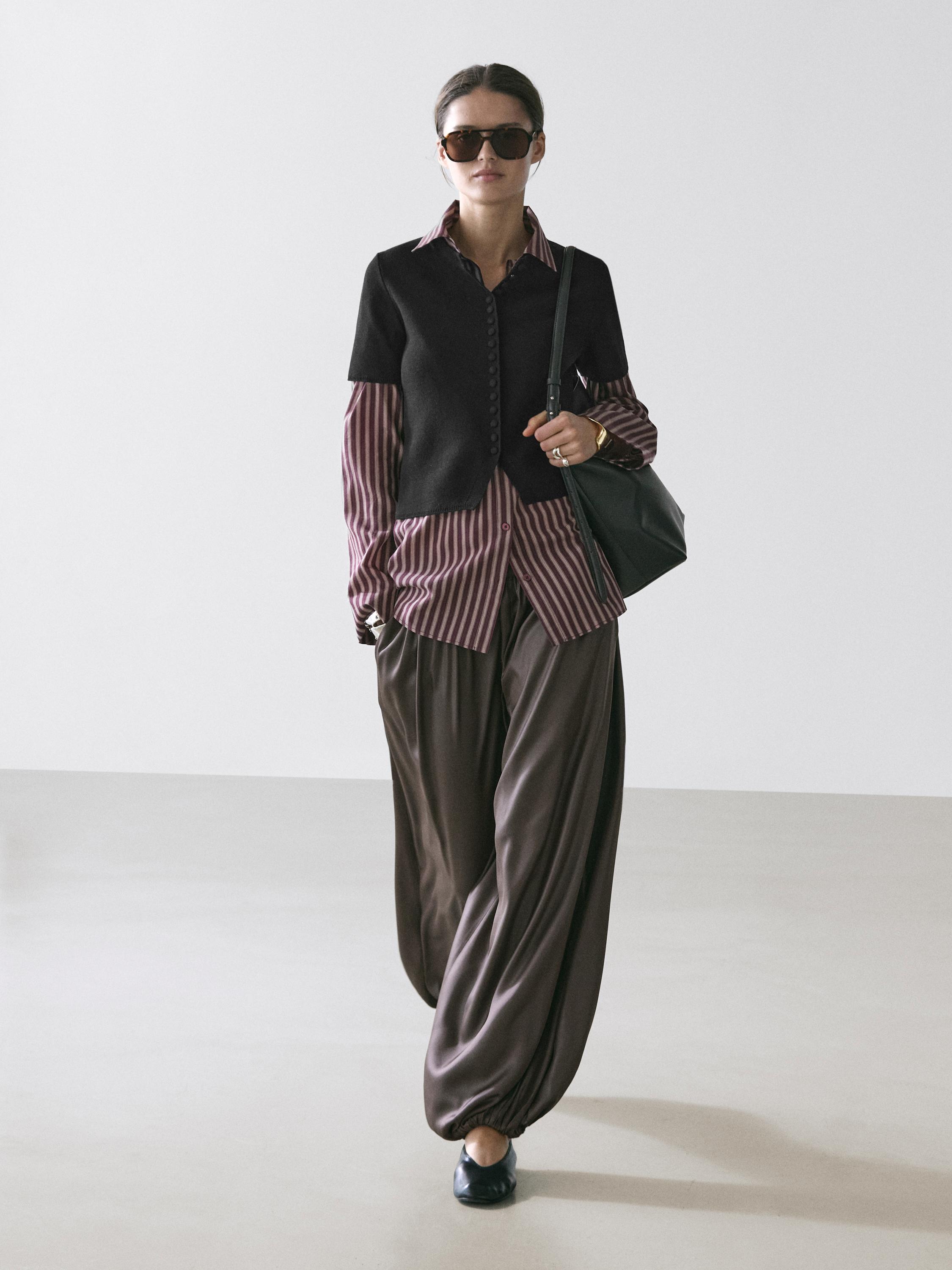 Set aus schwarzer Strickjacke mit kurzen Ärmeln über gestreiftem Hemd und brauner weiter Hose.