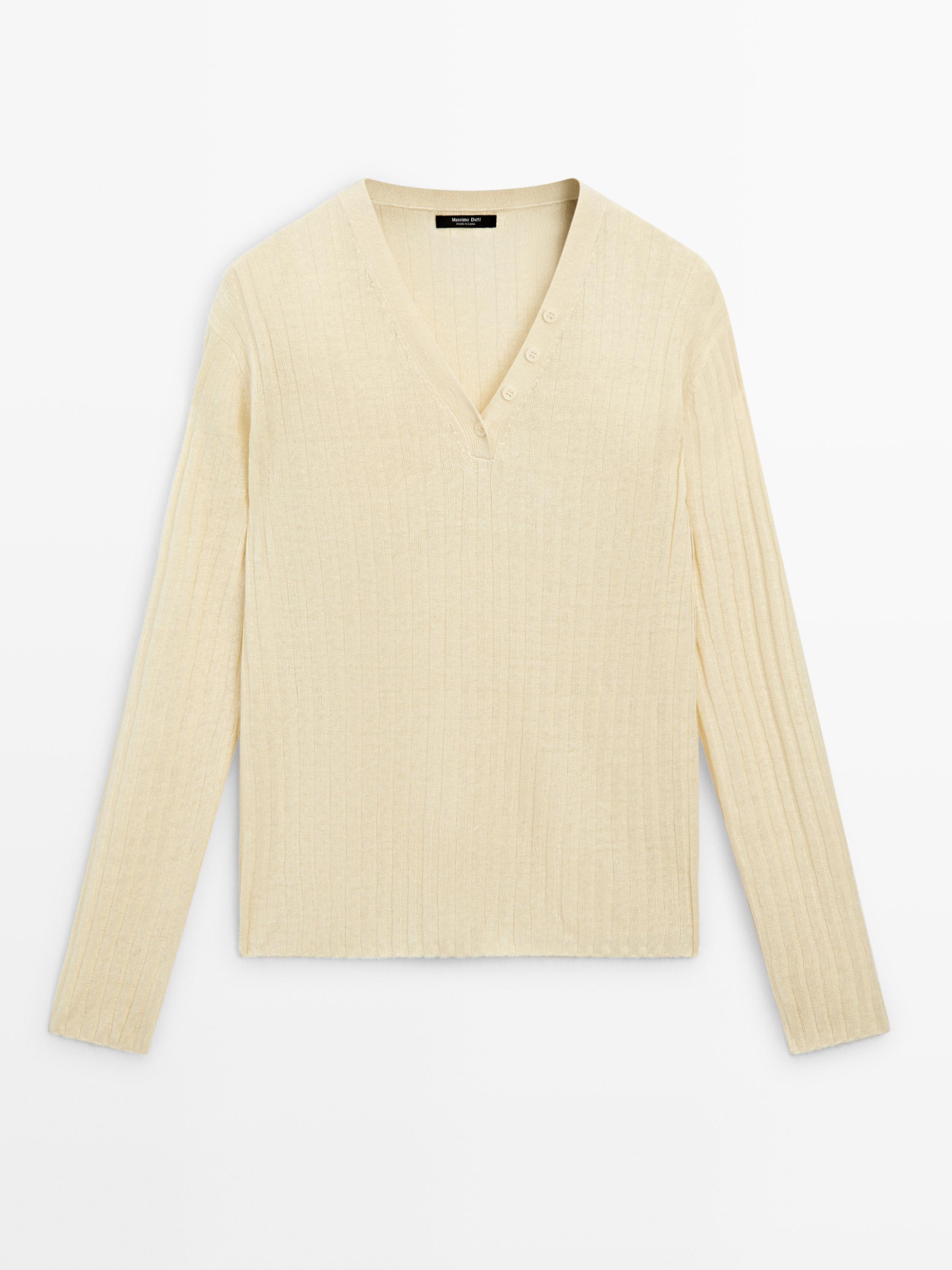 Vue frontale d'un pull vanille en maille avec col en V et détails boutonnés à l'encolure. Manches longues et texture côtelée.