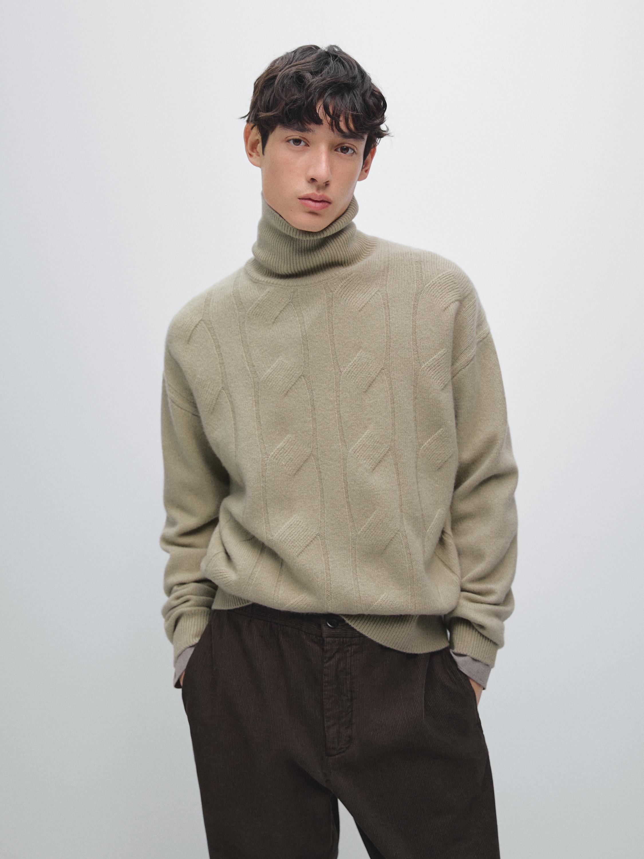 Conjunto de jersey beige de punto trenzado con cuello alto y pantalones oscuros.